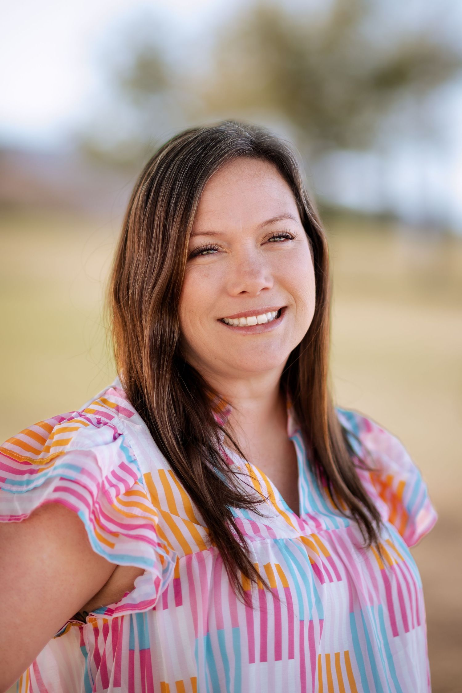 Outdoor portrait of a smiling person wearing a colorful striped blouse with pink, orange and blue patterns.
