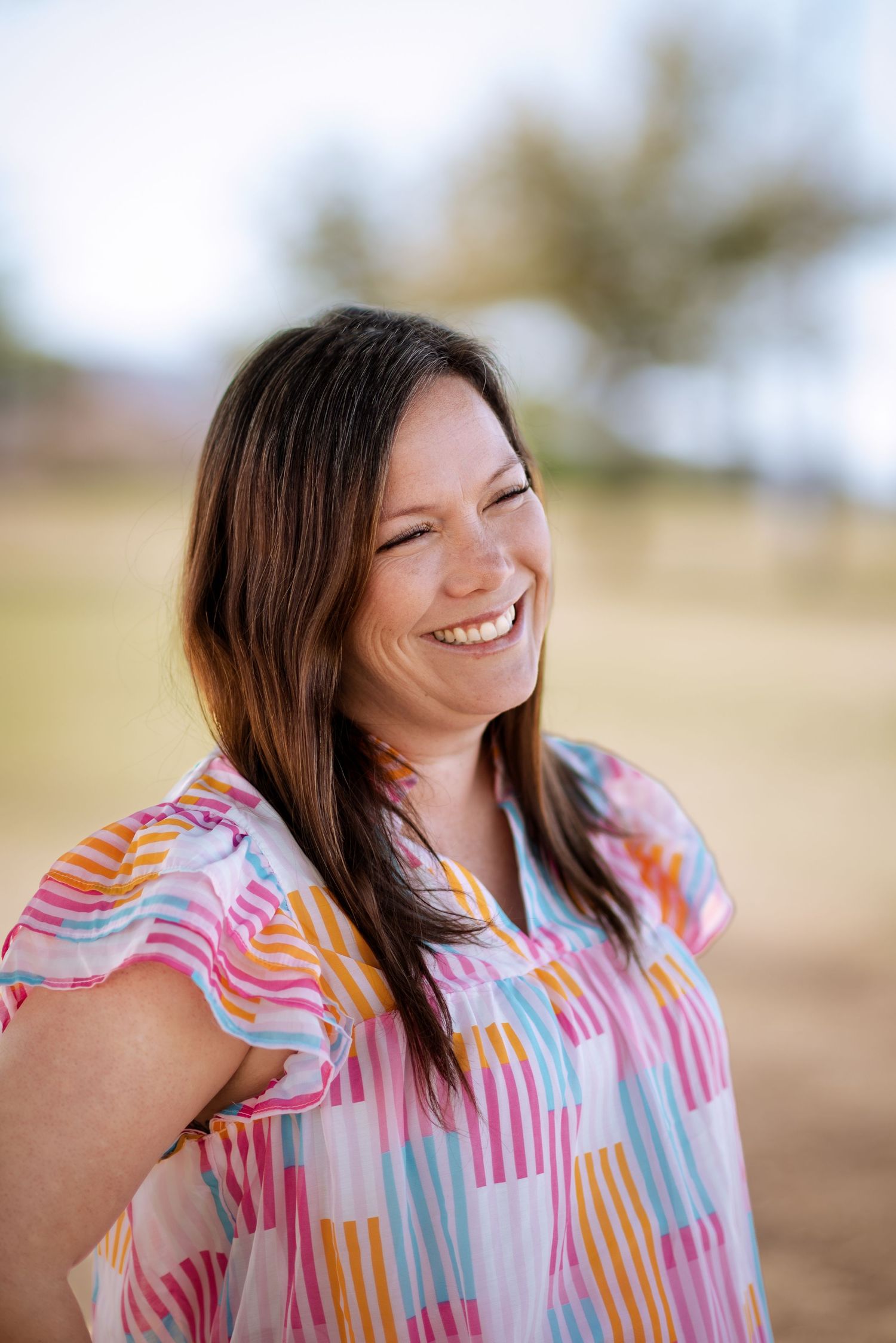 A candid portrait shows a joyful expression while wearing a colorful patterned blouse outdoors on a sunny day.