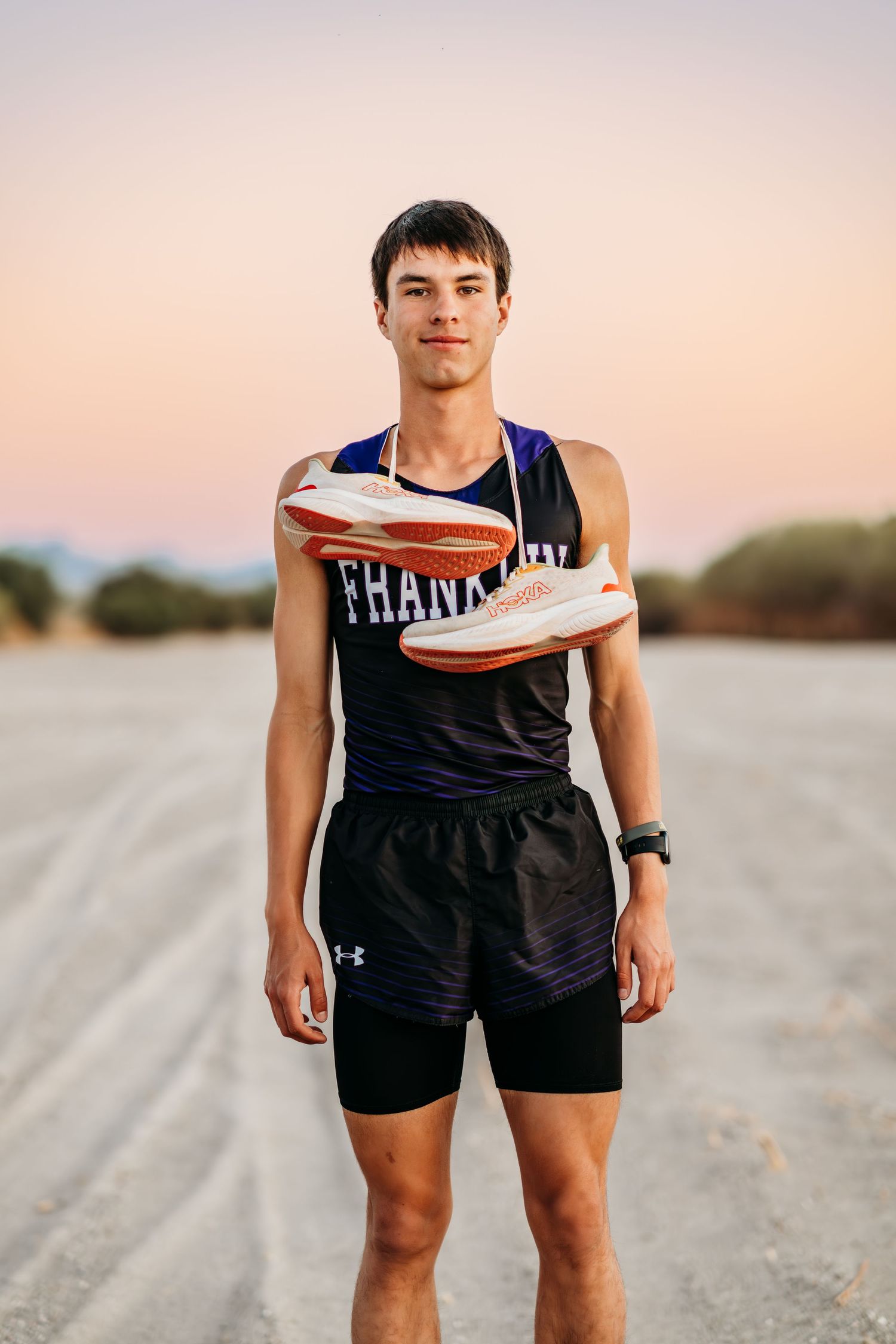 Athlete in Franklin uniform holds running shoes during sunset photoshoot.