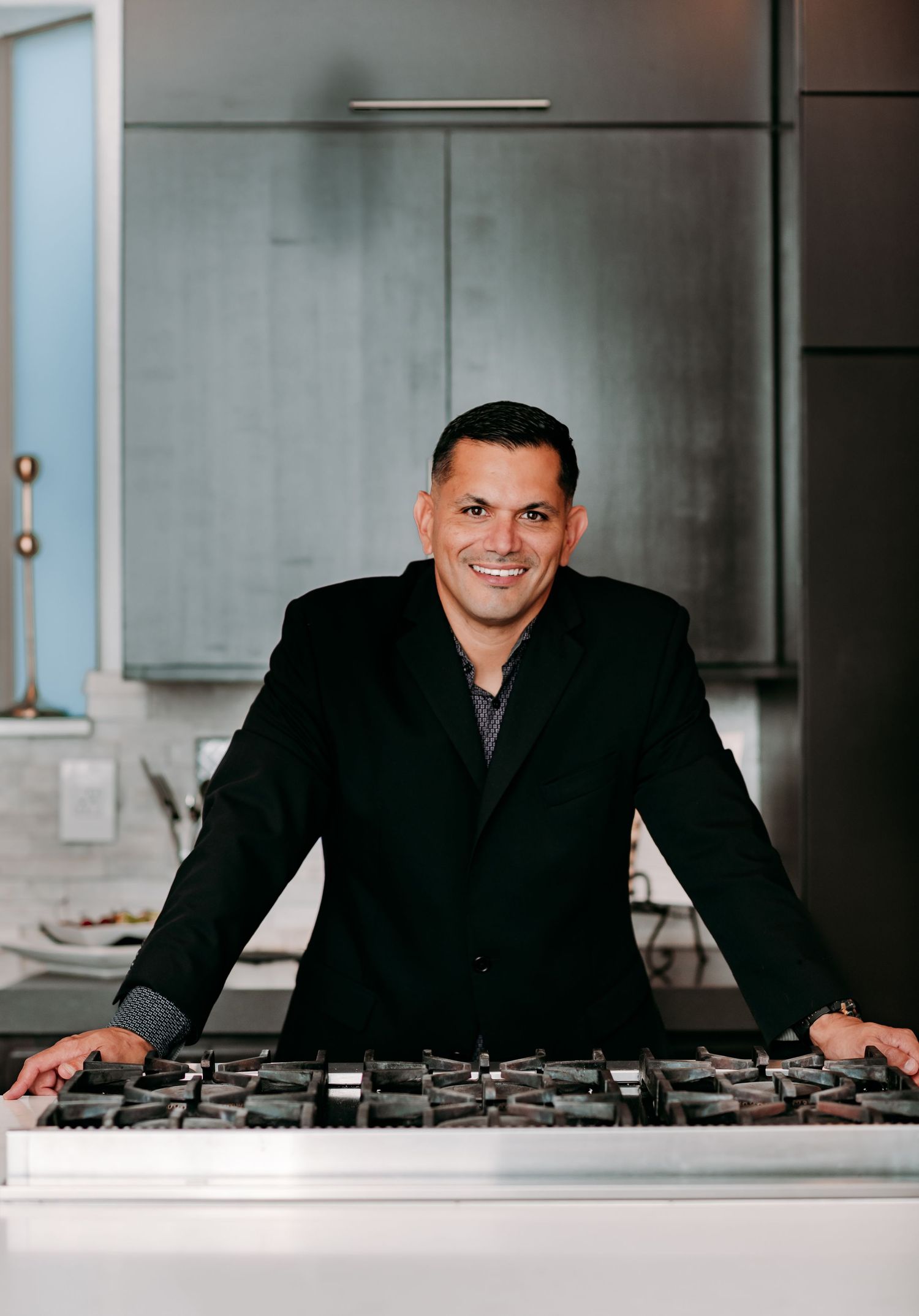 Professional chef stands behind a modern stainless steel gas cooktop in an upscale kitchen.