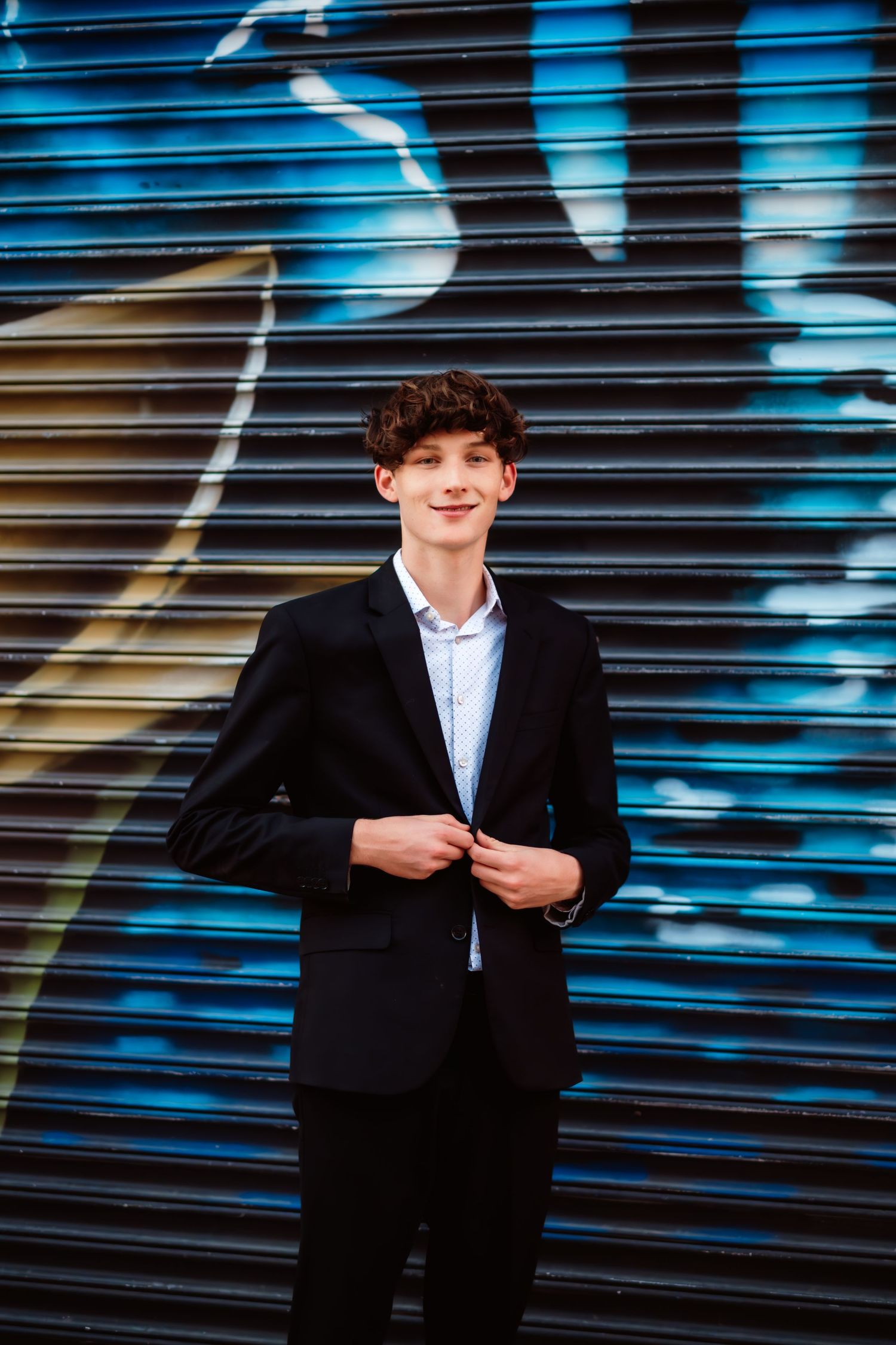 Portrait against blue industrial shutters wearing formal black attire.