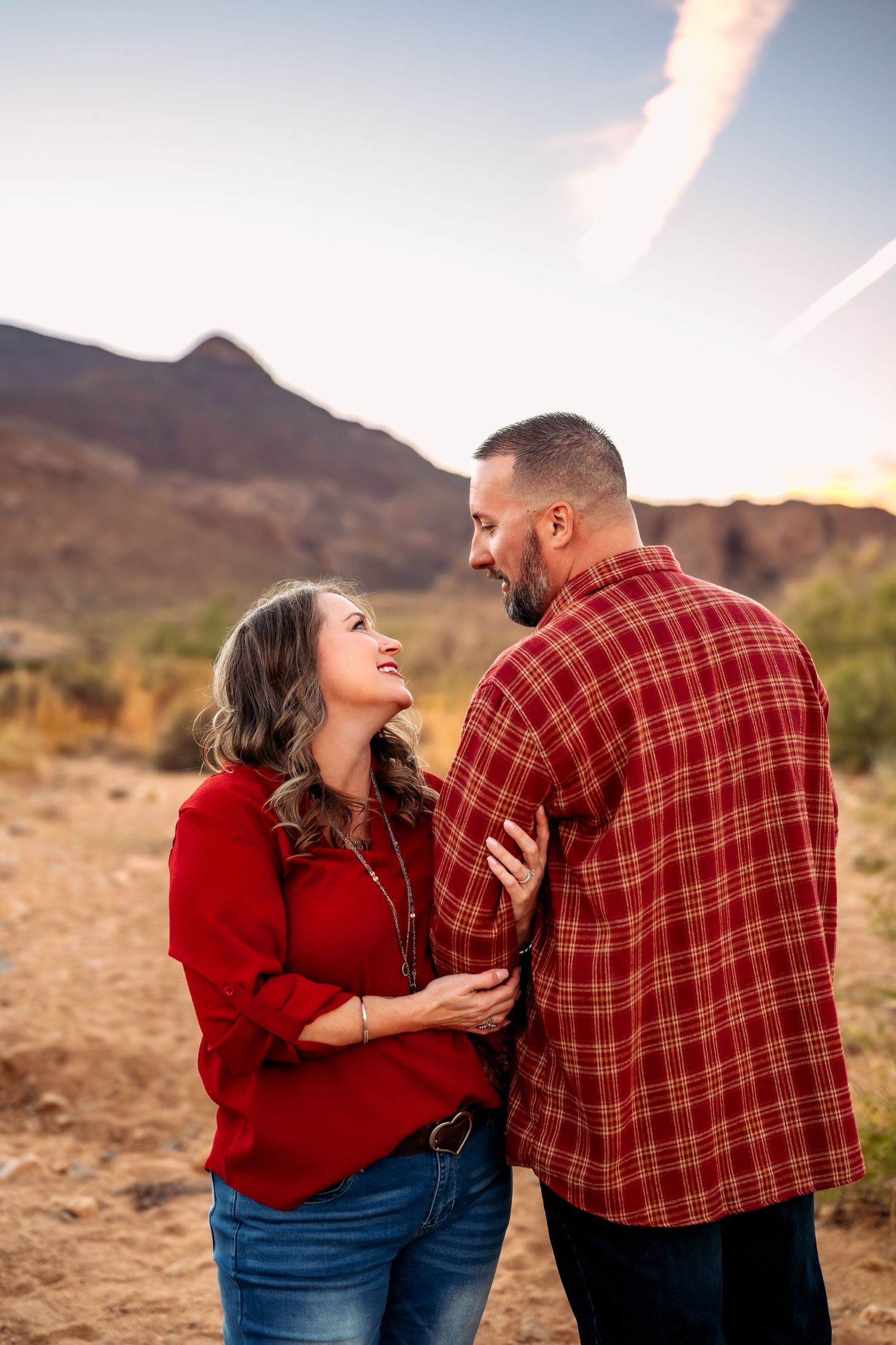 A couple shares a laugh in the desert wearing red and plaid outfits with mountains in the background.