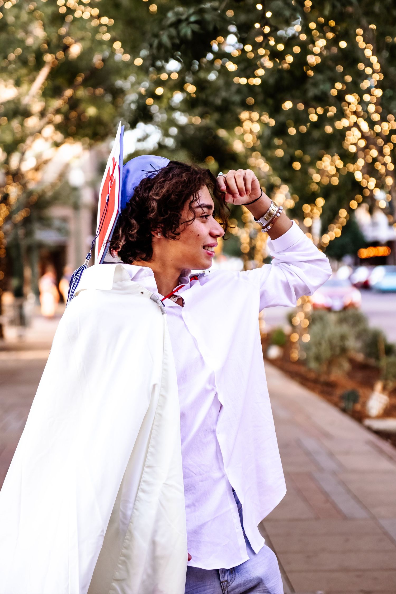 Person wearing a white shirt and cape poses outdoors with twinkling bokeh lights in the background.