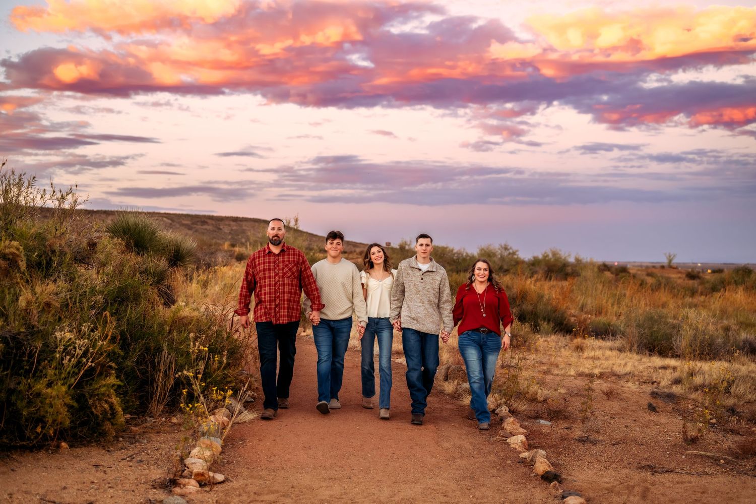 Family photo shoot against dramatic pink and purple sunset sky in desert landscape.