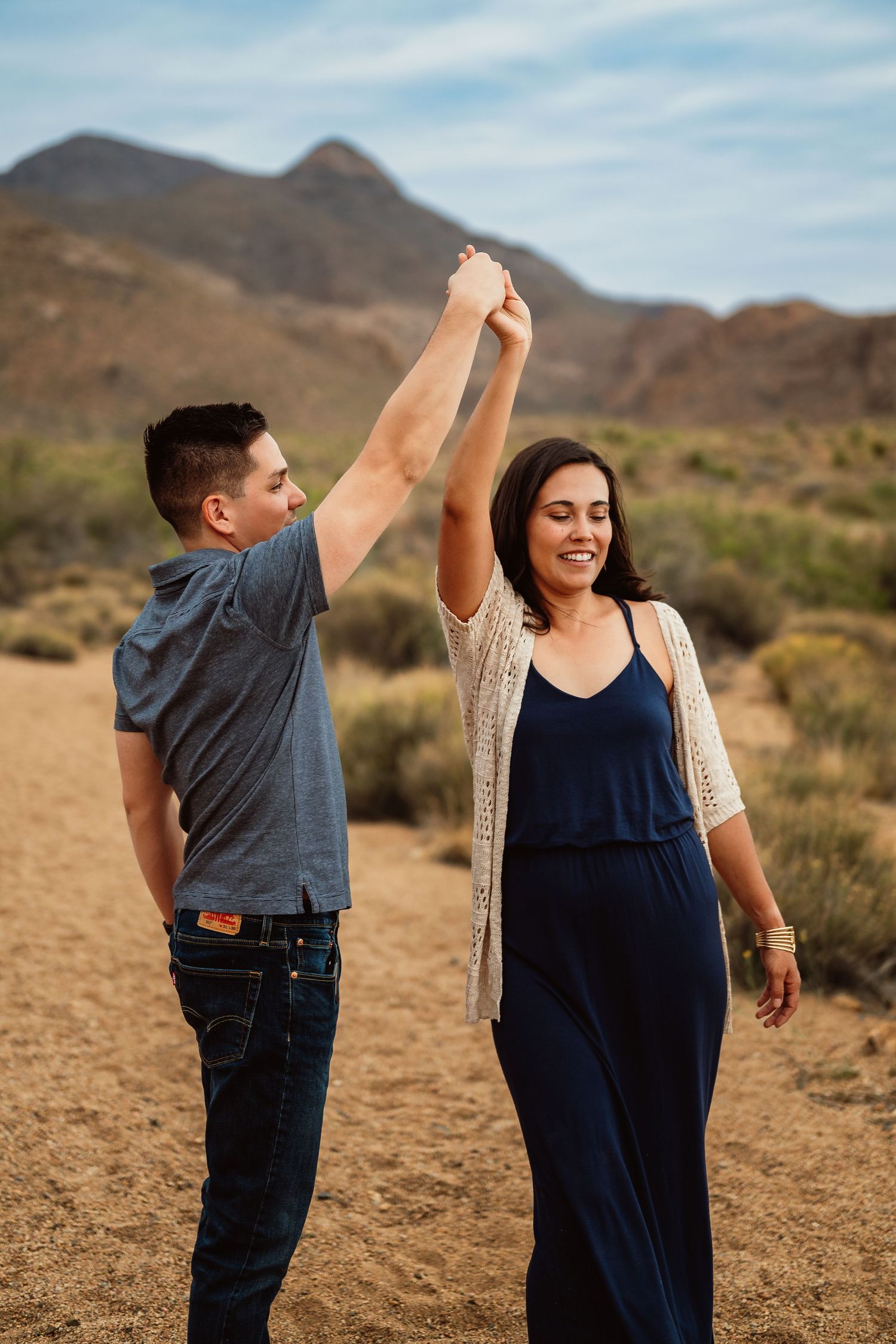 A playful moment captured in the desert with casual outfits against a mountain backdrop.