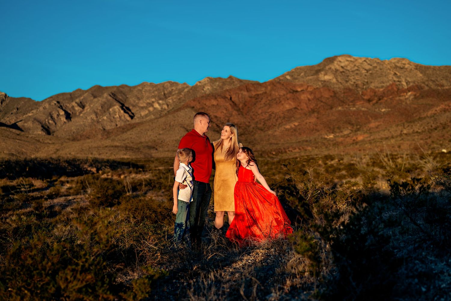 A family poses together against rocky mountains during sunset.