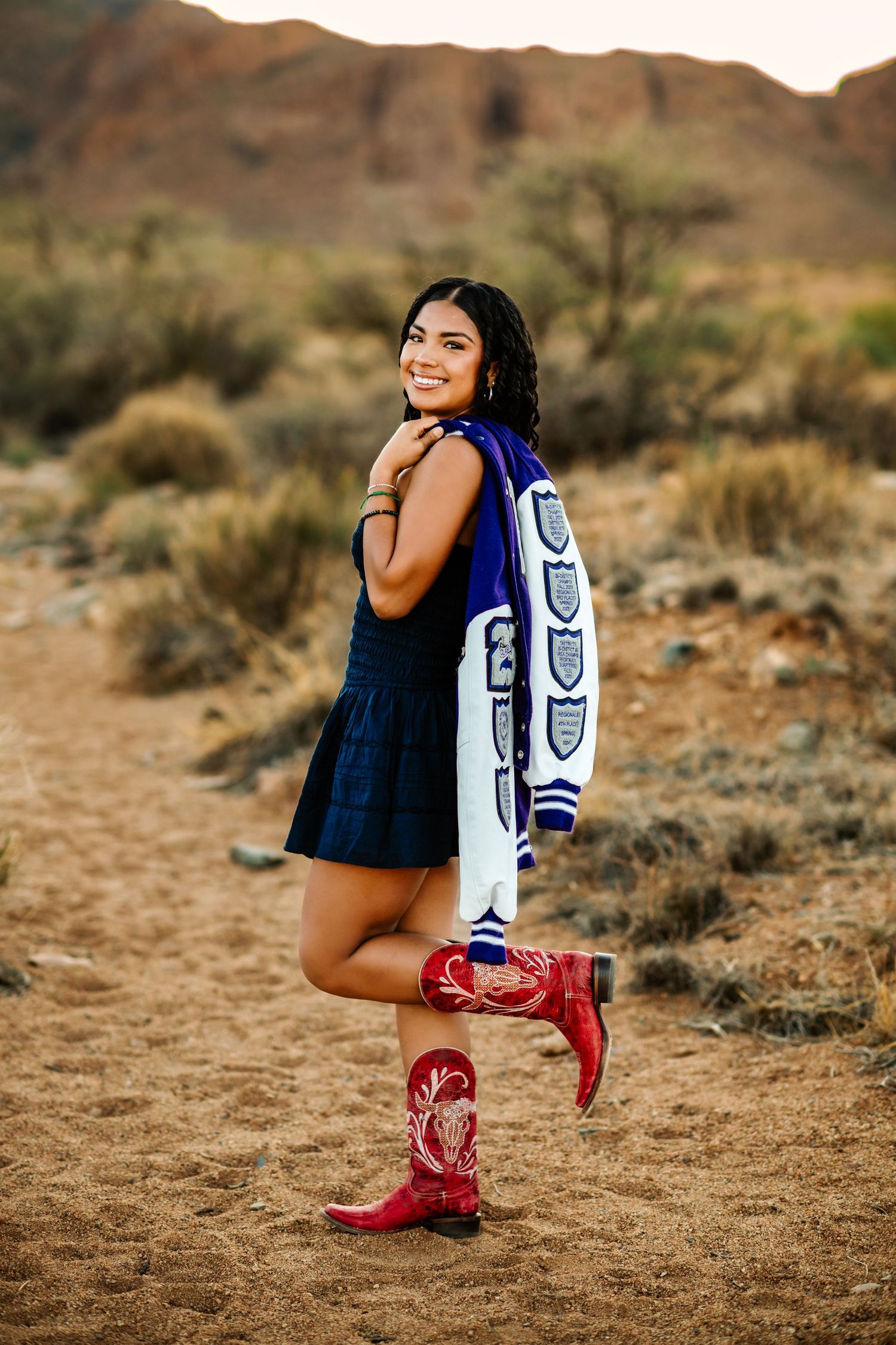 Playful desert photoshoot featuring red cowboy boots and varsity jacket.