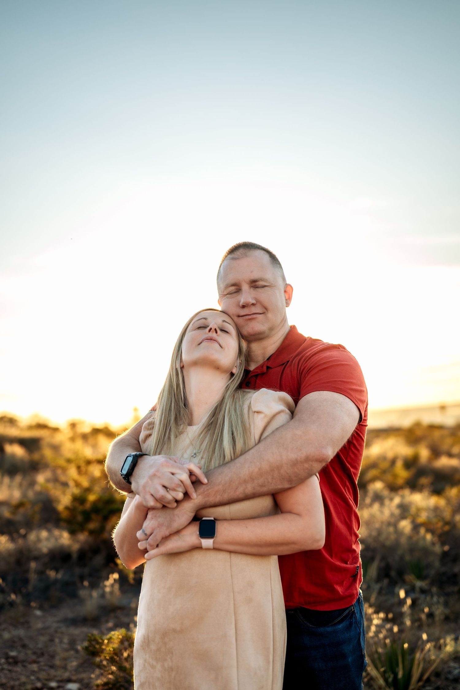 A couple embraces while laughing together in a desert landscape during sunset.