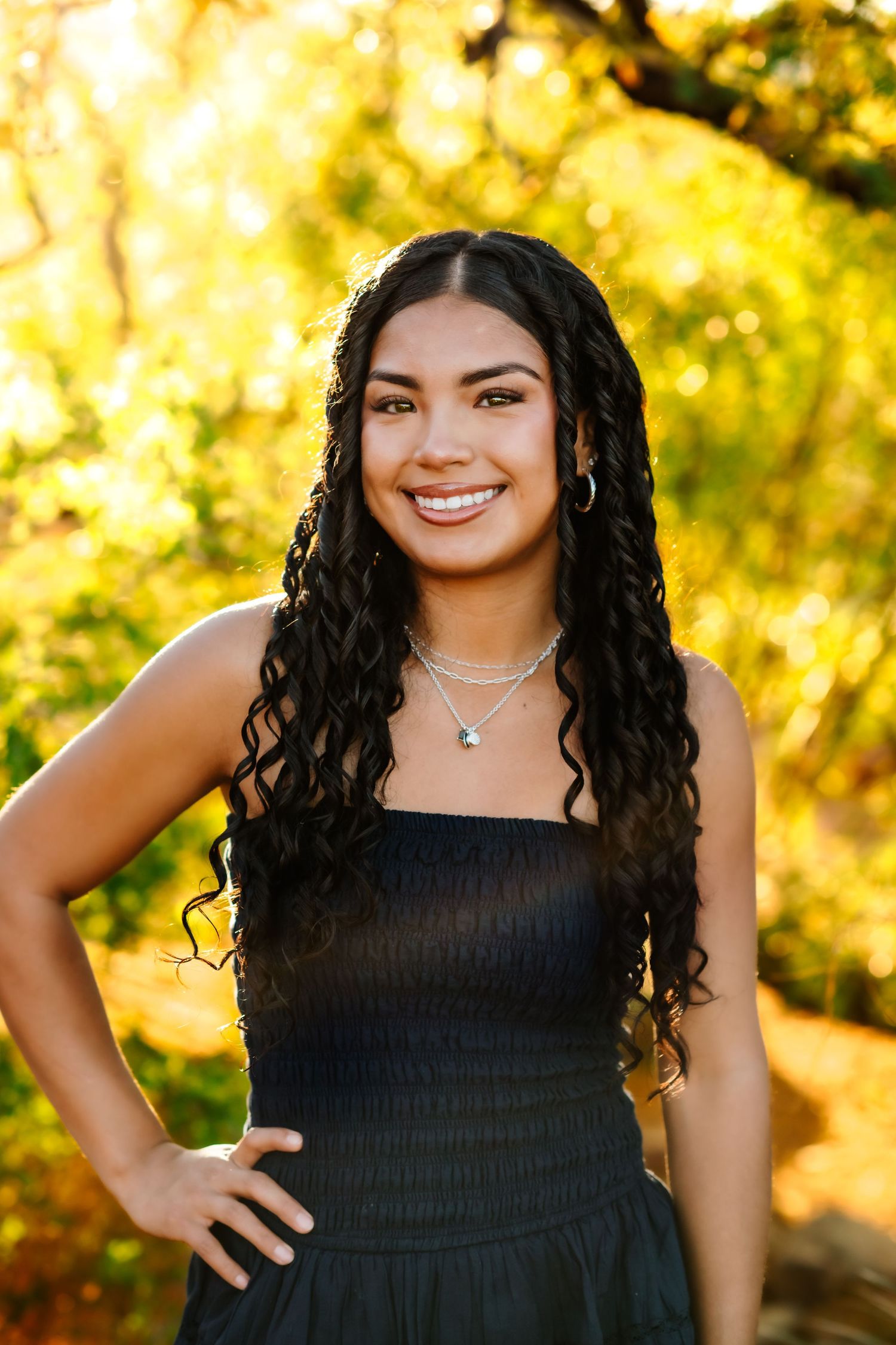 Portrait of young woman in black dress with curly hair against golden autumn background.