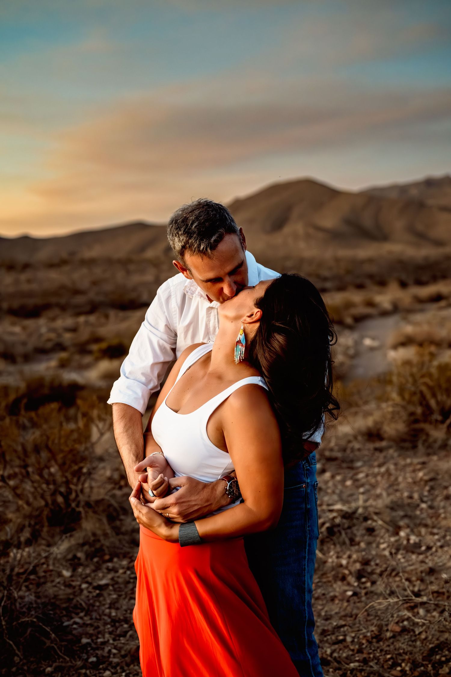 Couple embraces in desert landscape during sunset.