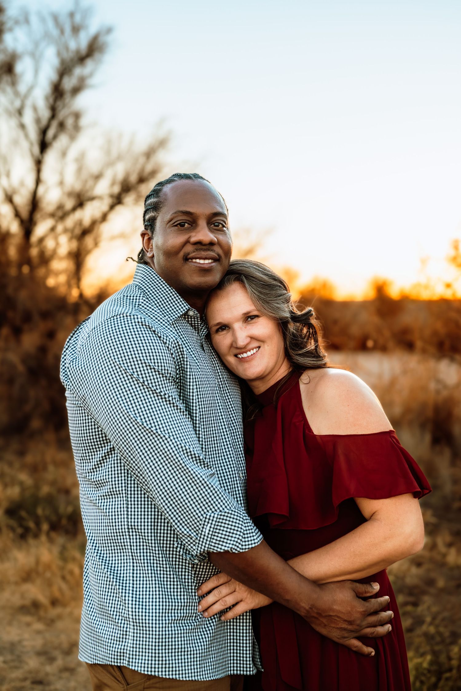 A couple embraces and laughs together in a field during golden sunset hour.
