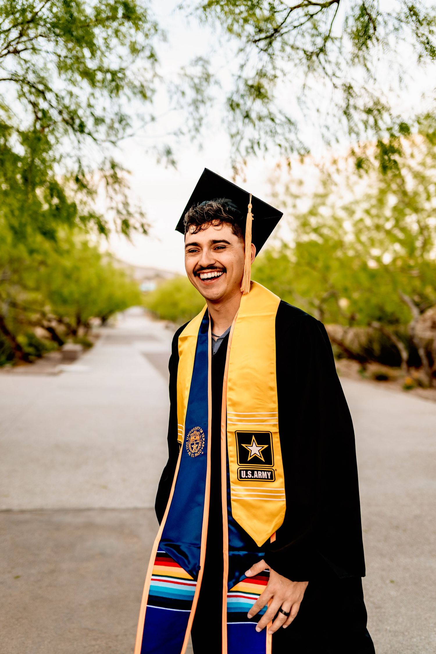 A graduate in cap and gown with yellow stole smiles during outdoor graduation photos.