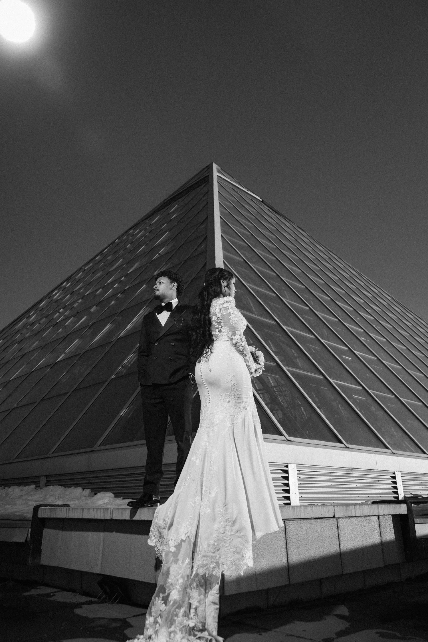 Black and white wedding portrait with geometric pyramid architecture and bright sunlight.
