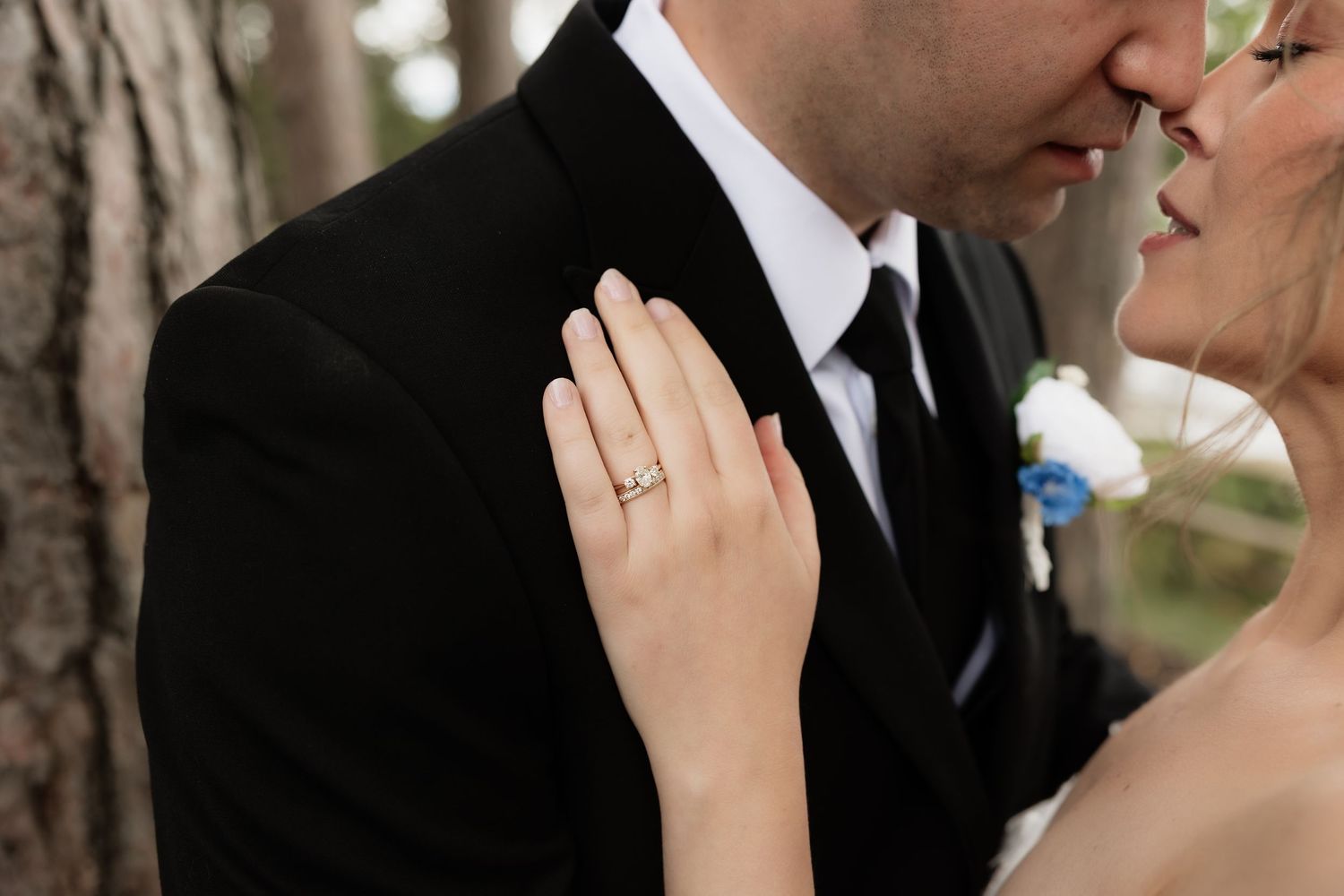 Bride and groom sharing a kiss, showcasing a diamond engagement ring on her hand, with the groom in a black tuxedo.