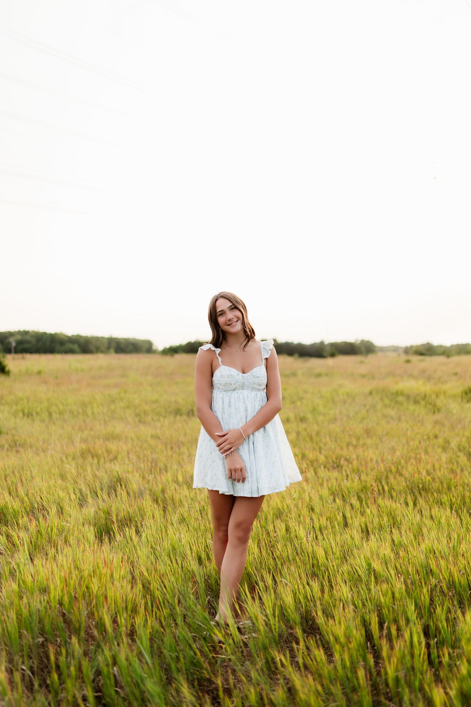 Young woman in white sundress standing in an open golden field under an overcast sky.