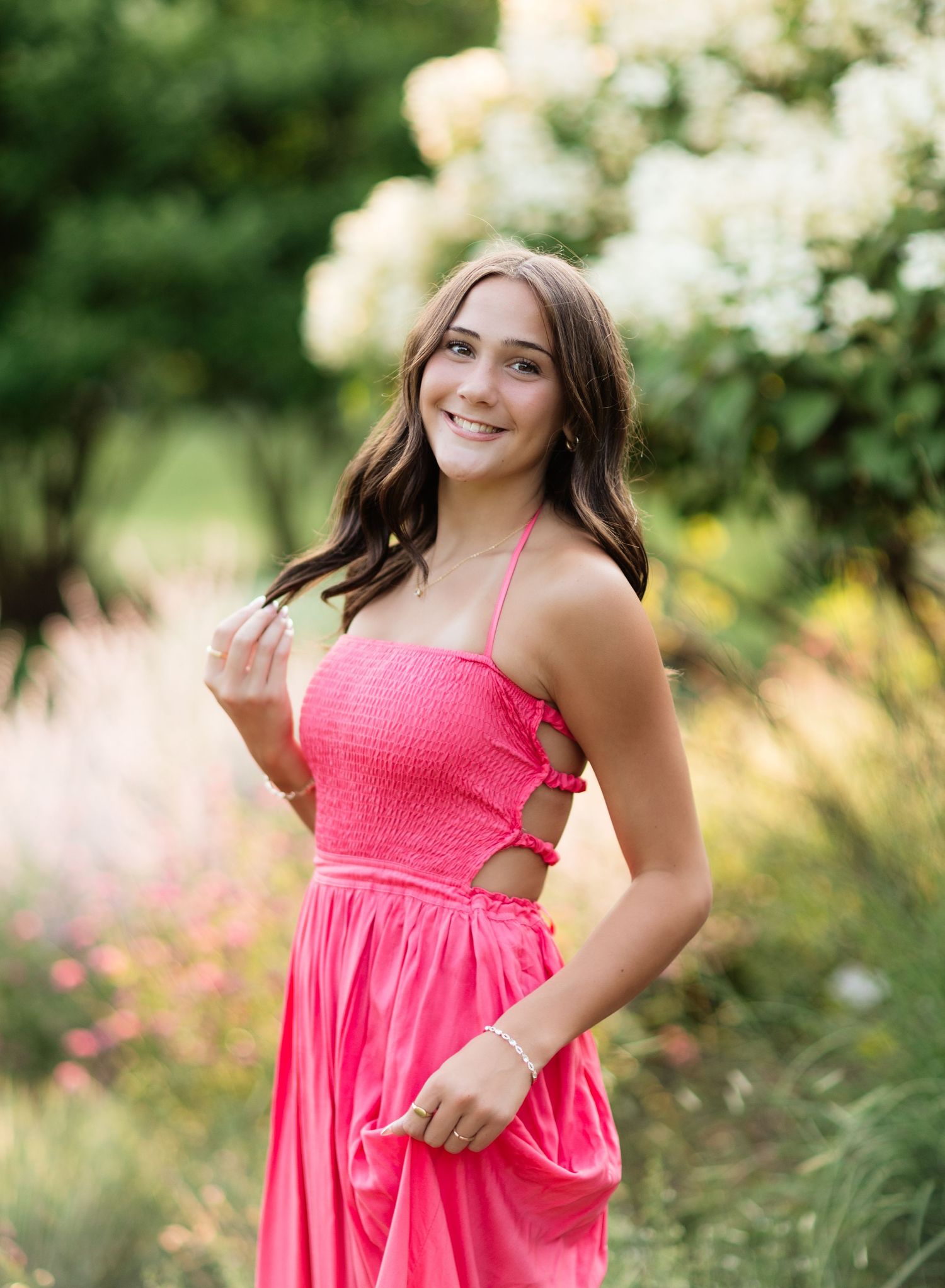 Happy young woman in hot pink halter maxi dress with cutout detail standing in garden.