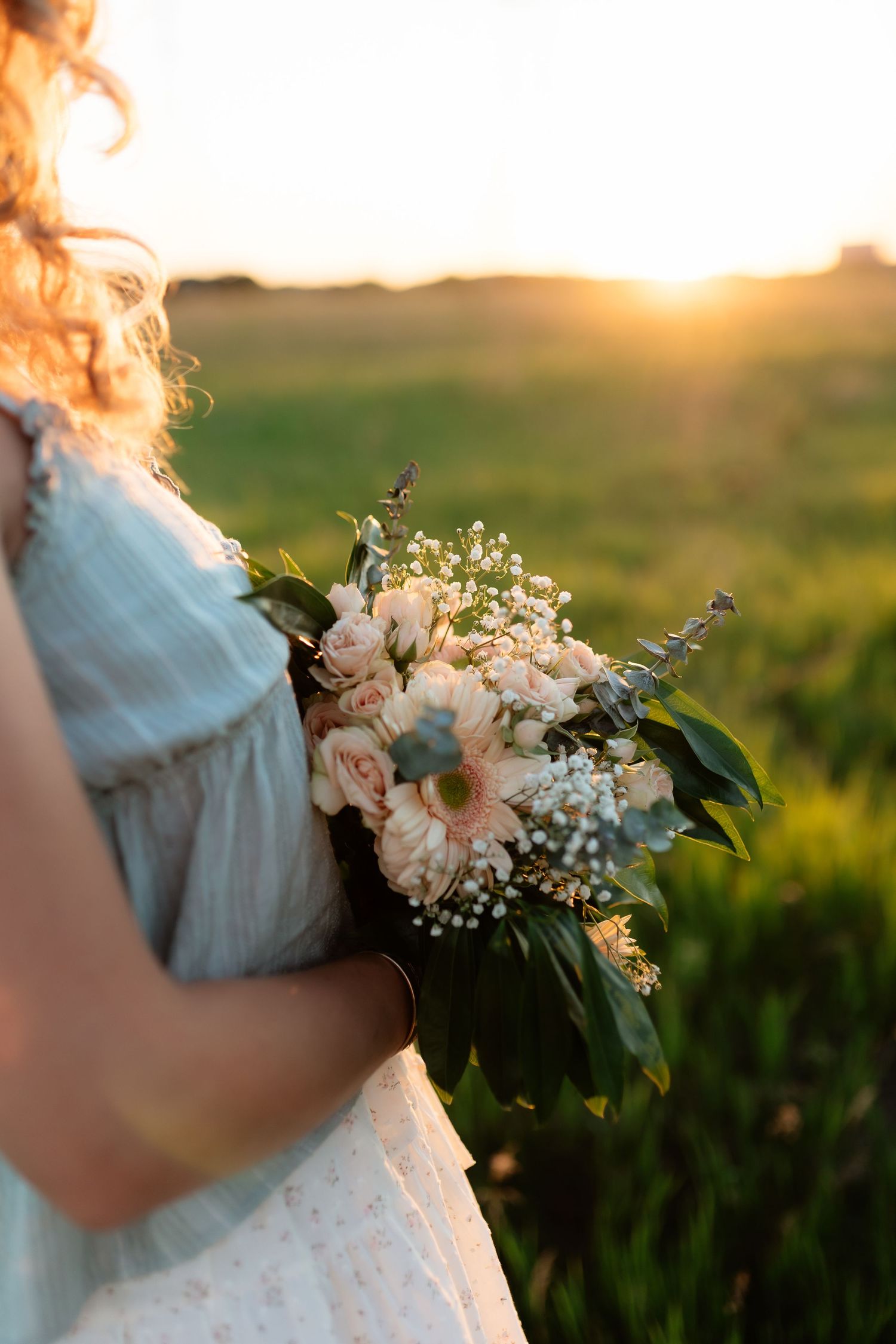 Close-up of a beautiful bridal bouquet with pink roses and white flowers held at golden sunset.