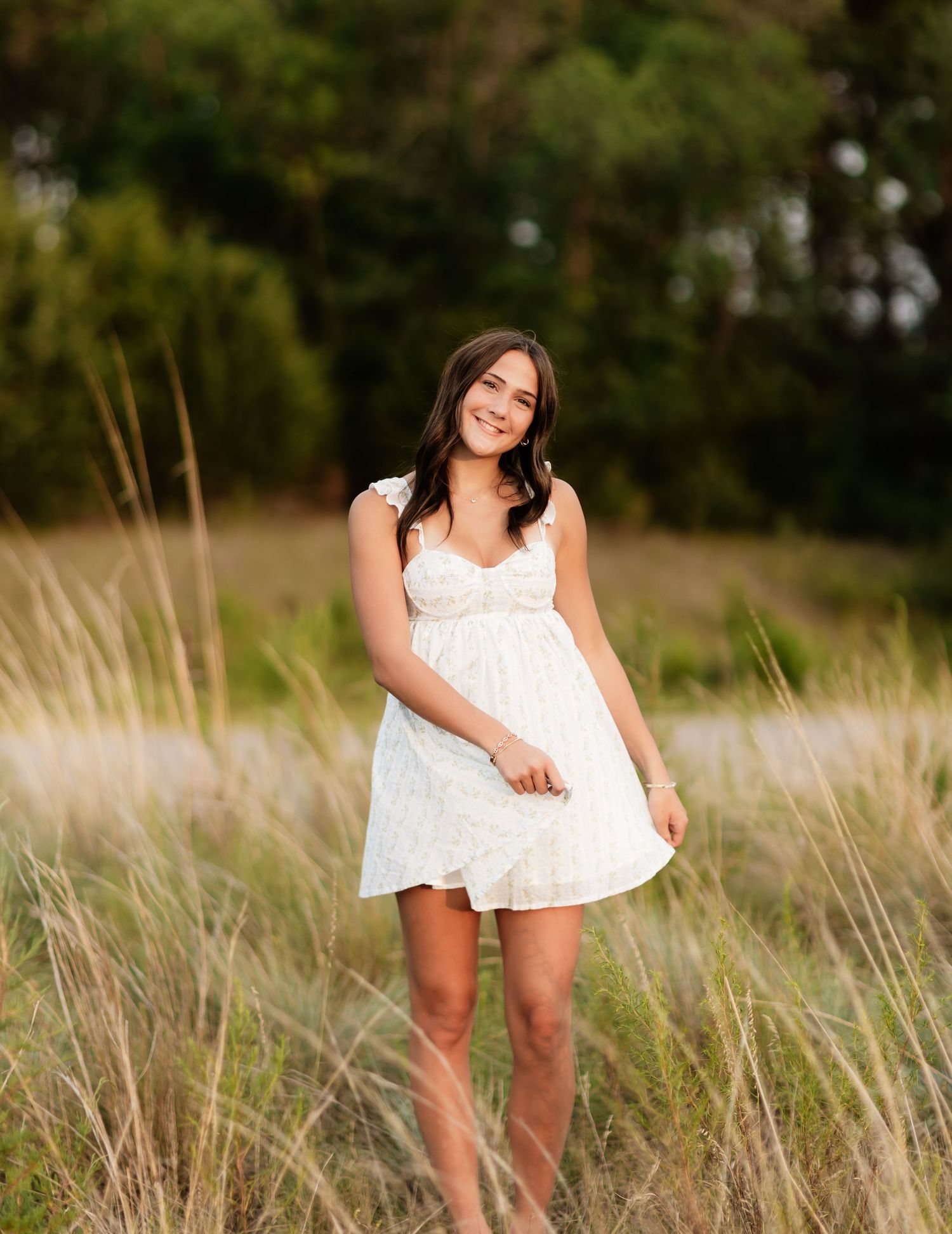 Smiling young woman in white lace dress standing in tall golden grass field.