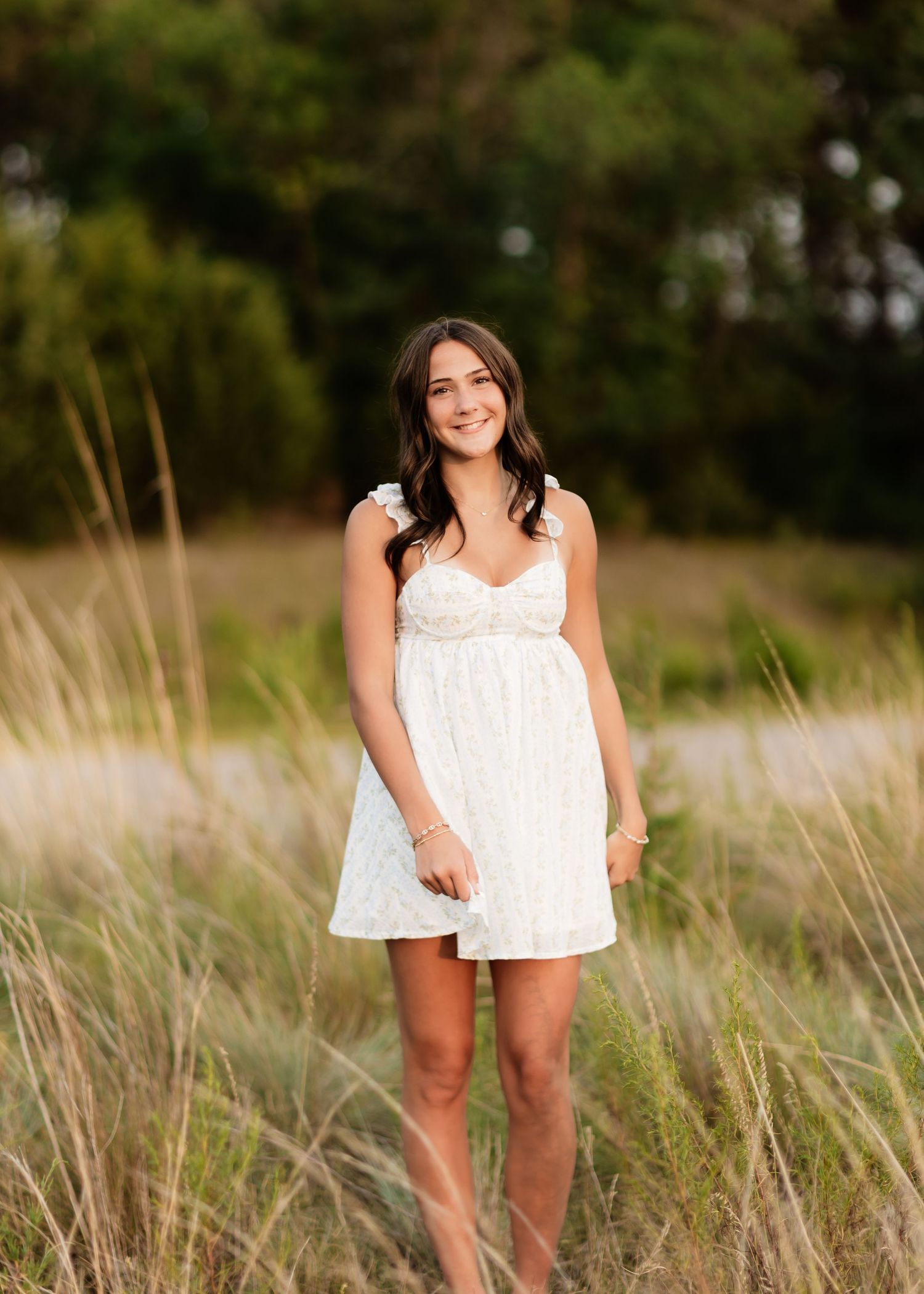 Teen girl in white lace dress standing in tall golden meadow grass outdoors.