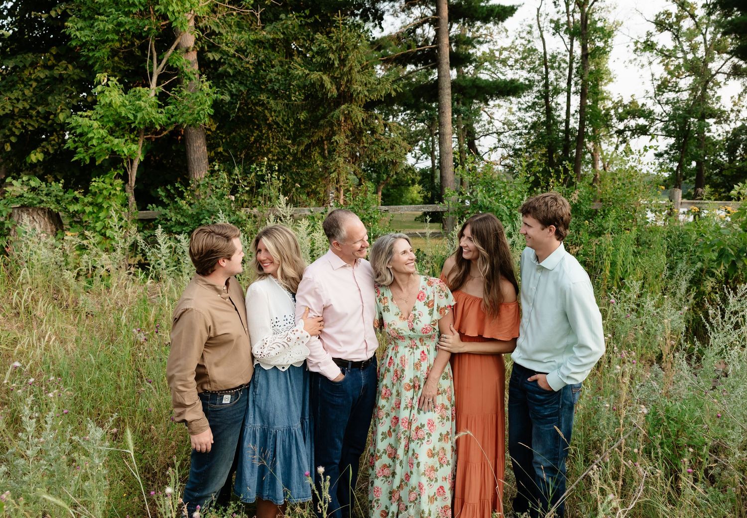 Family of six smiling and laughing together outdoors in a lush green garden during a professional family portrait session.