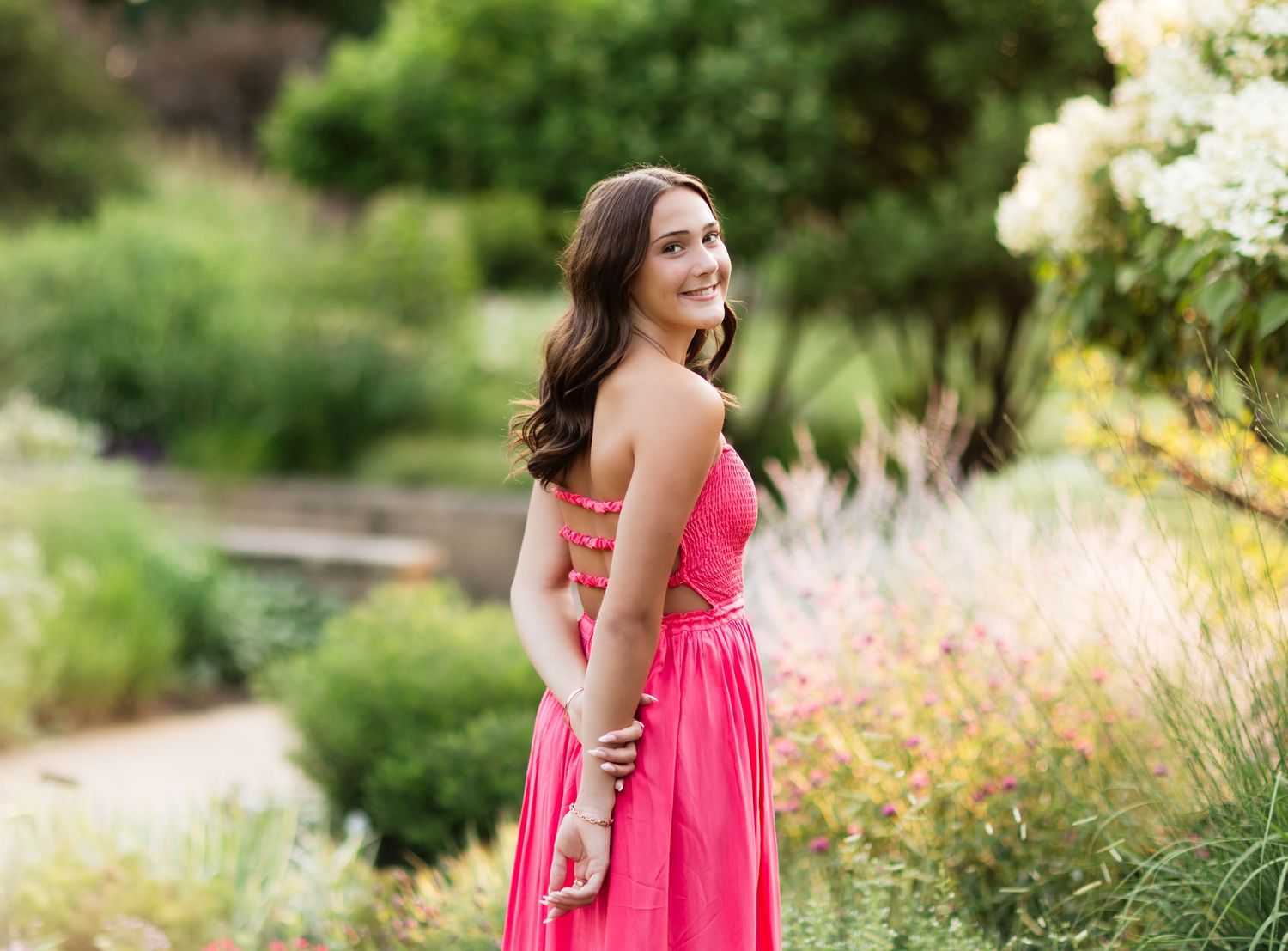 Smiling brunette in pink strapless dress standing in colorful garden landscape.