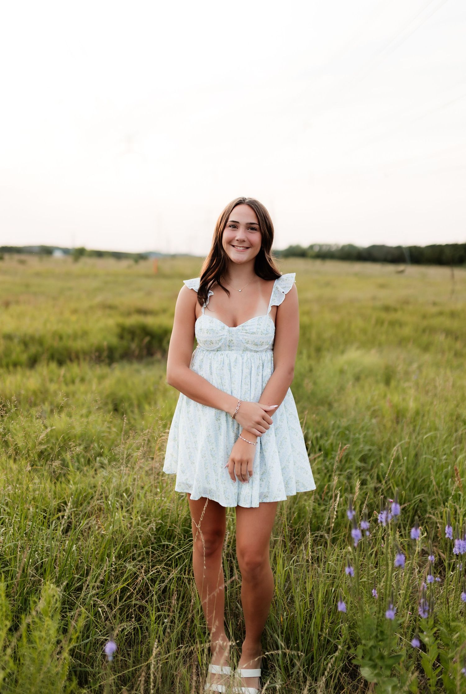 Young woman in light blue floral dress smiling in wildflower meadow.