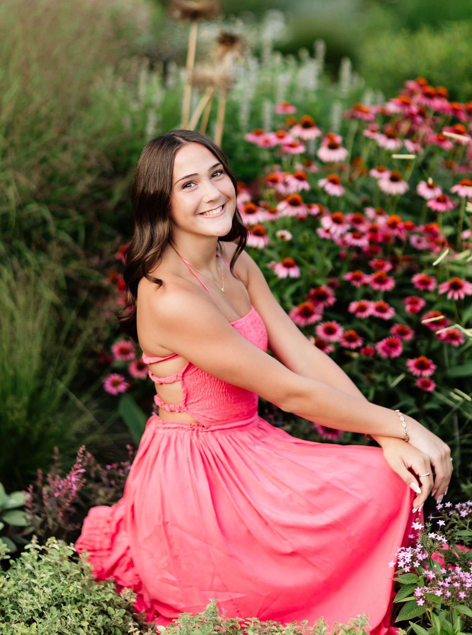 Young woman in coral pink dress smiling among vibrant pink echinacea flowers in a lush garden setting.