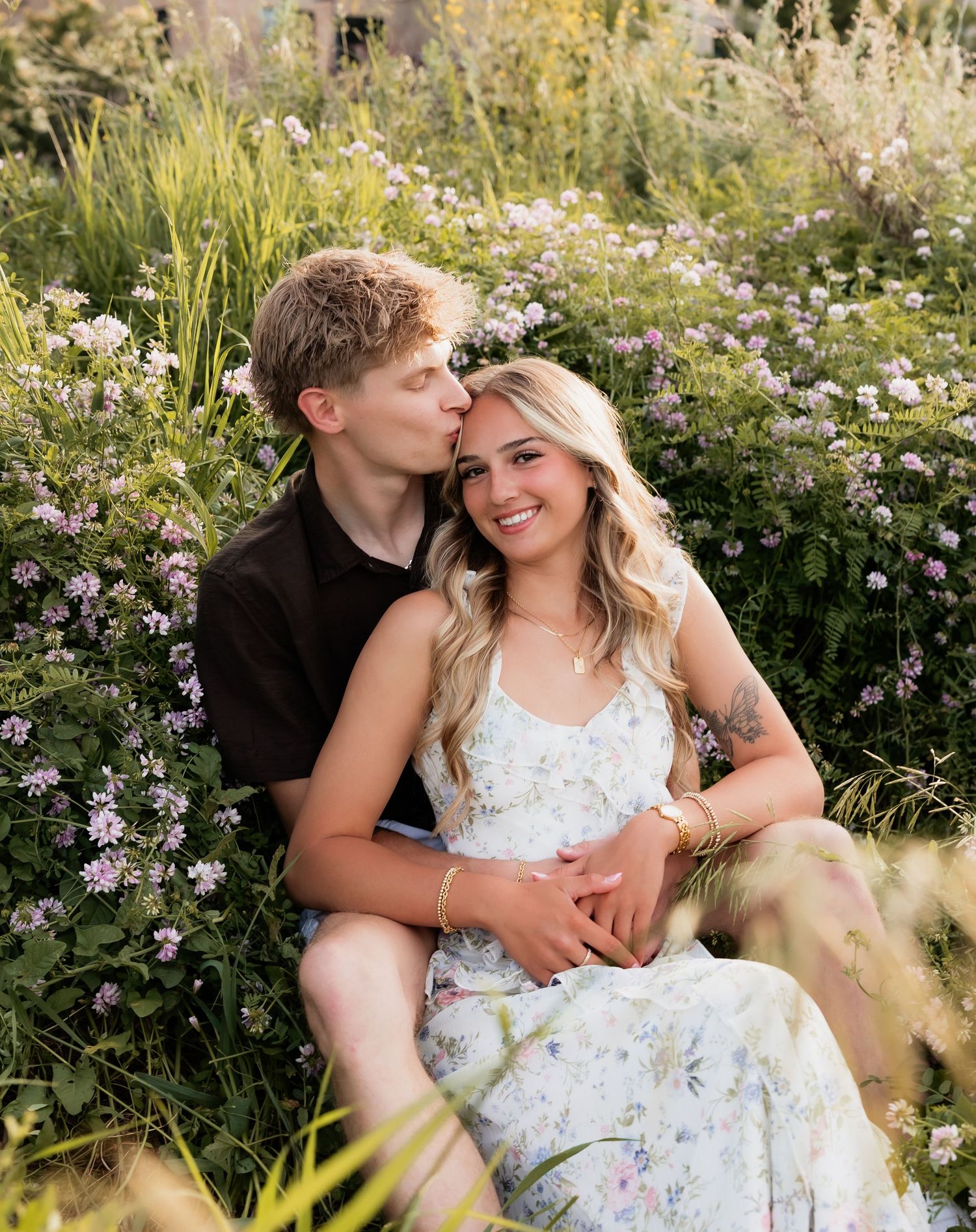 Happy couple sitting together in a field of wildflowers, sharing a tender moment outdoors.