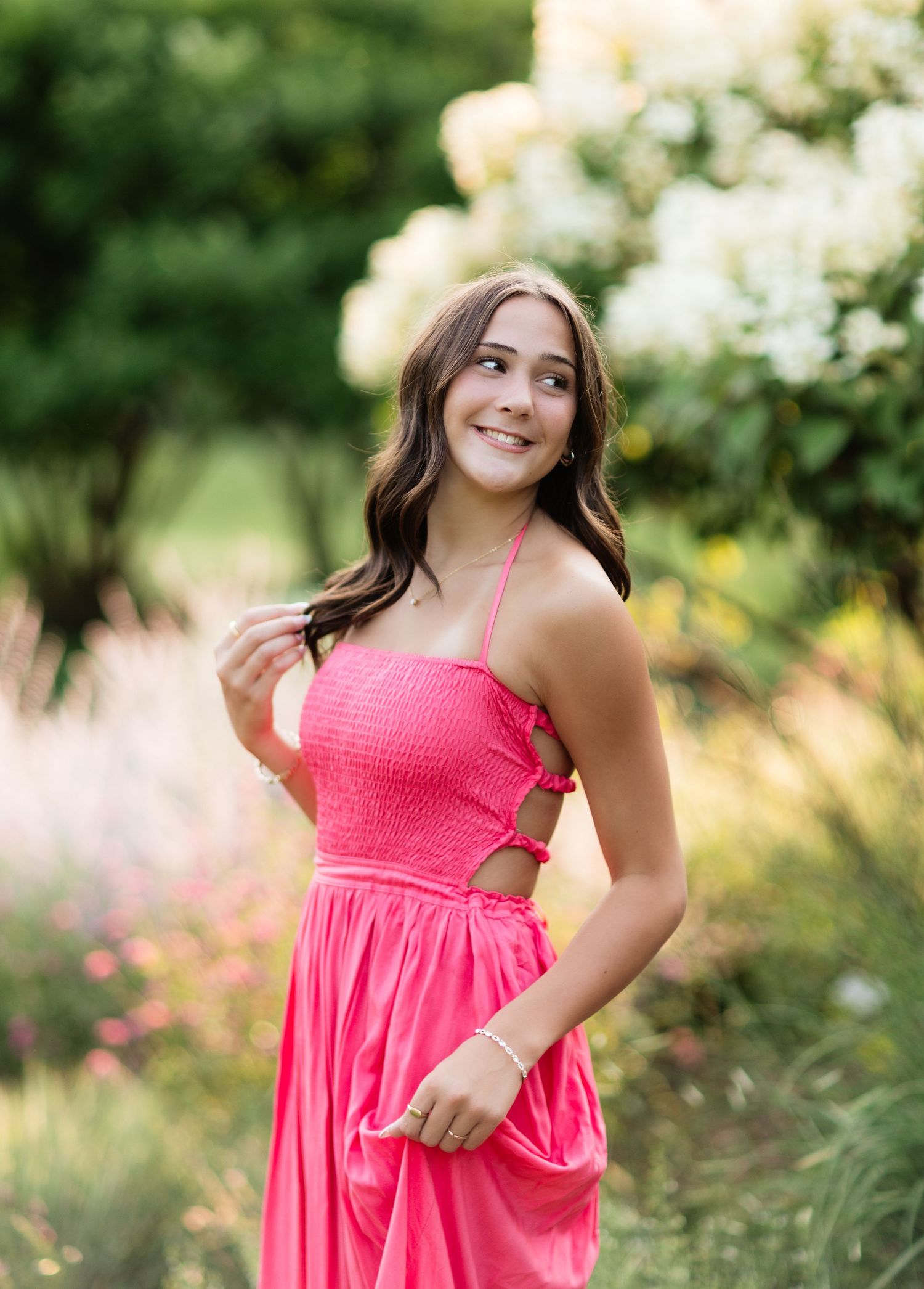 Young woman in a pink smocked halter dress smiling in a garden with white hydrangeas.