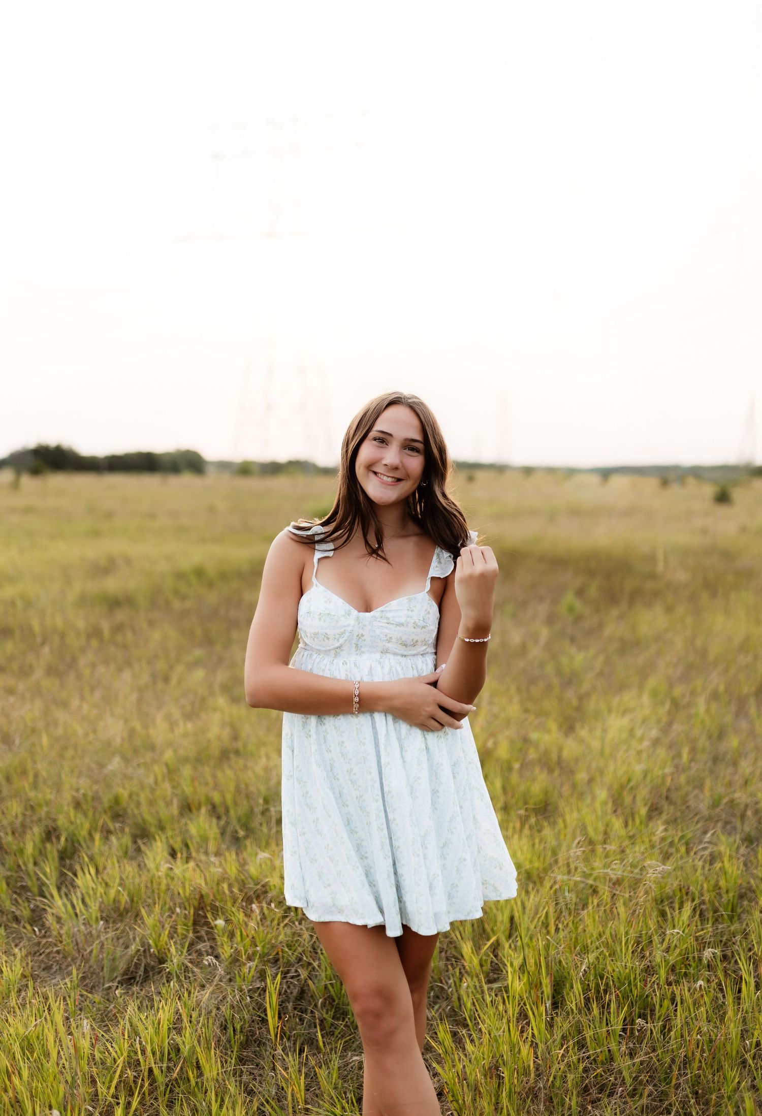 Young woman in white mini dress standing in an open grassy field.