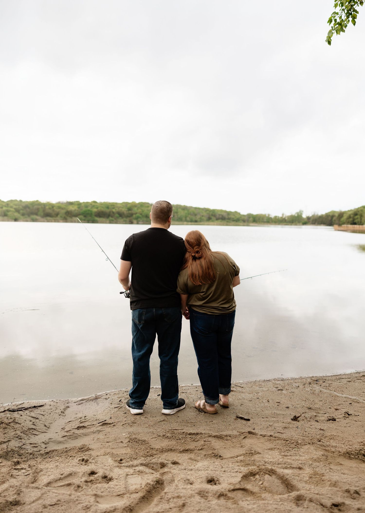 Couple fishing together on a sandy lakeshore, standing side by side with fishing rods.