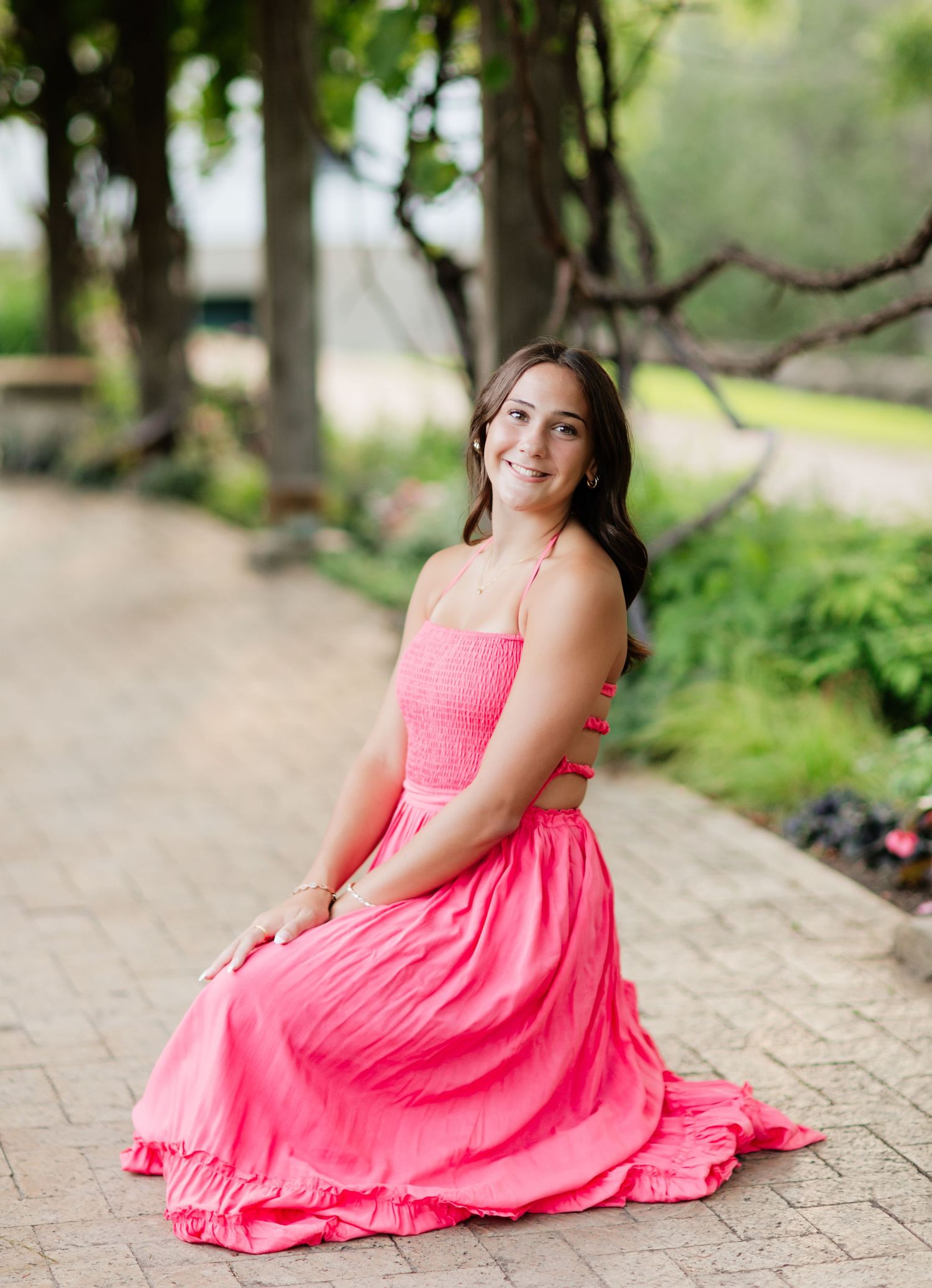 Young woman in pink dress sitting gracefully on a brick path in a garden.