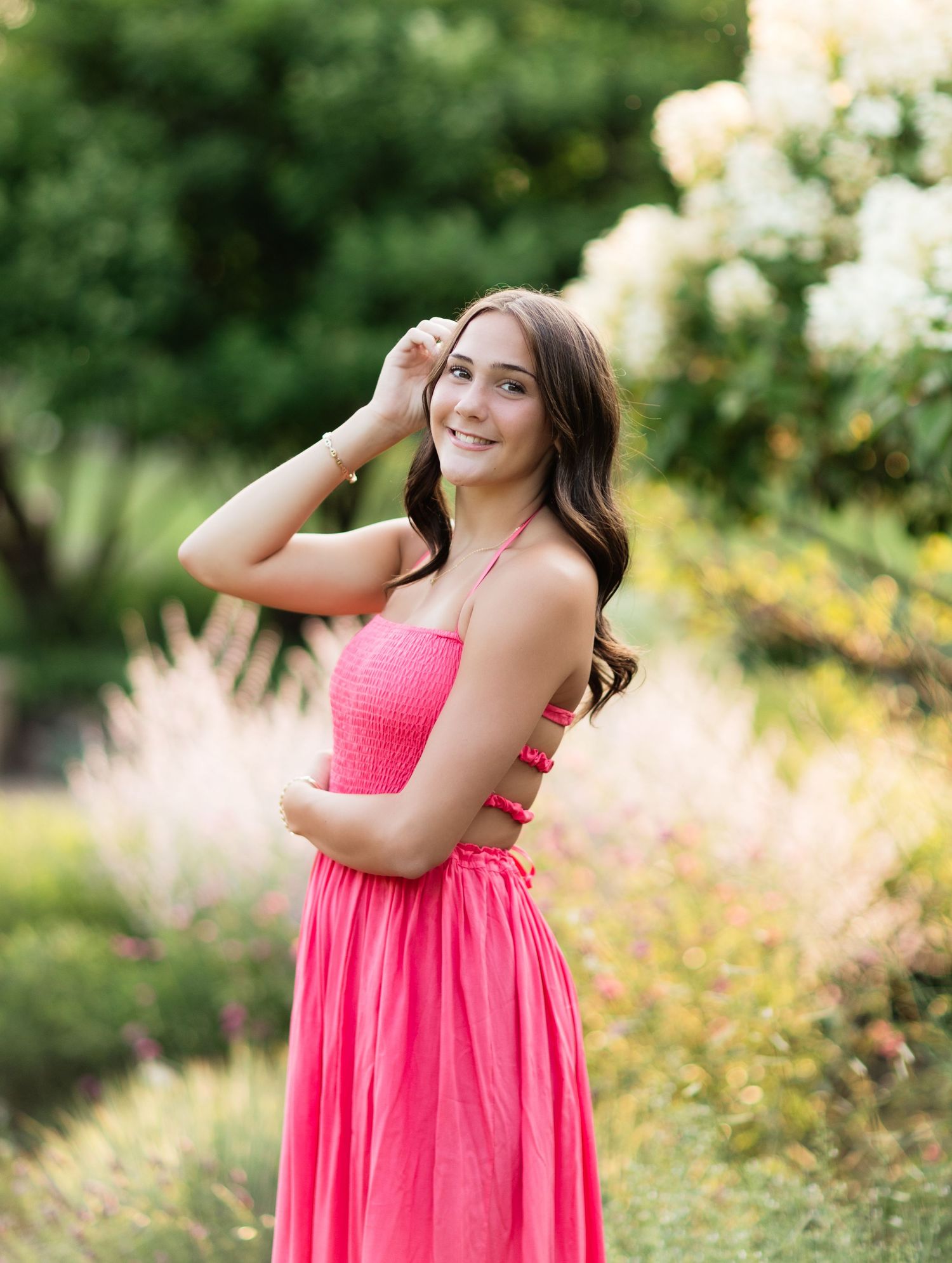 Smiling teen girl in bright pink smocked maxi dress posing in a lush garden with flowers.