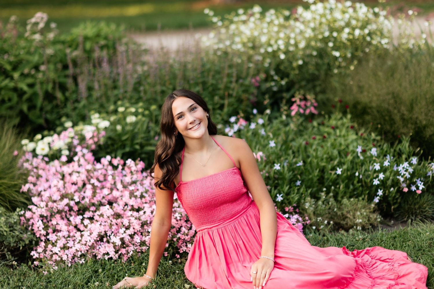 Smiling young woman in a pink strapless dress sitting in front of a colorful wildflower garden.