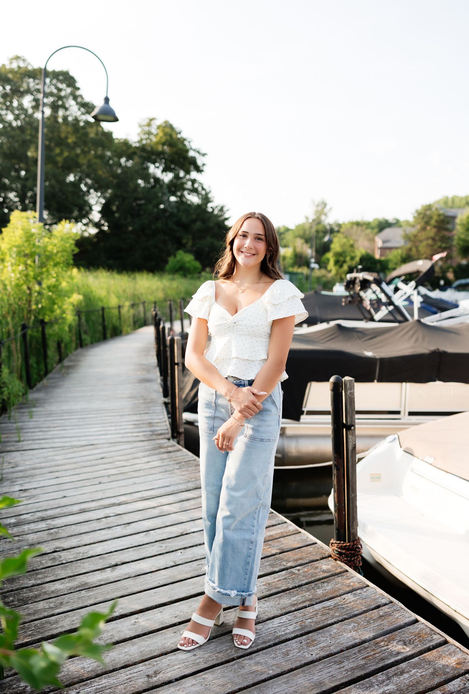 Smiling young woman in white top and jeans standing on a wooden marina dock in summer.