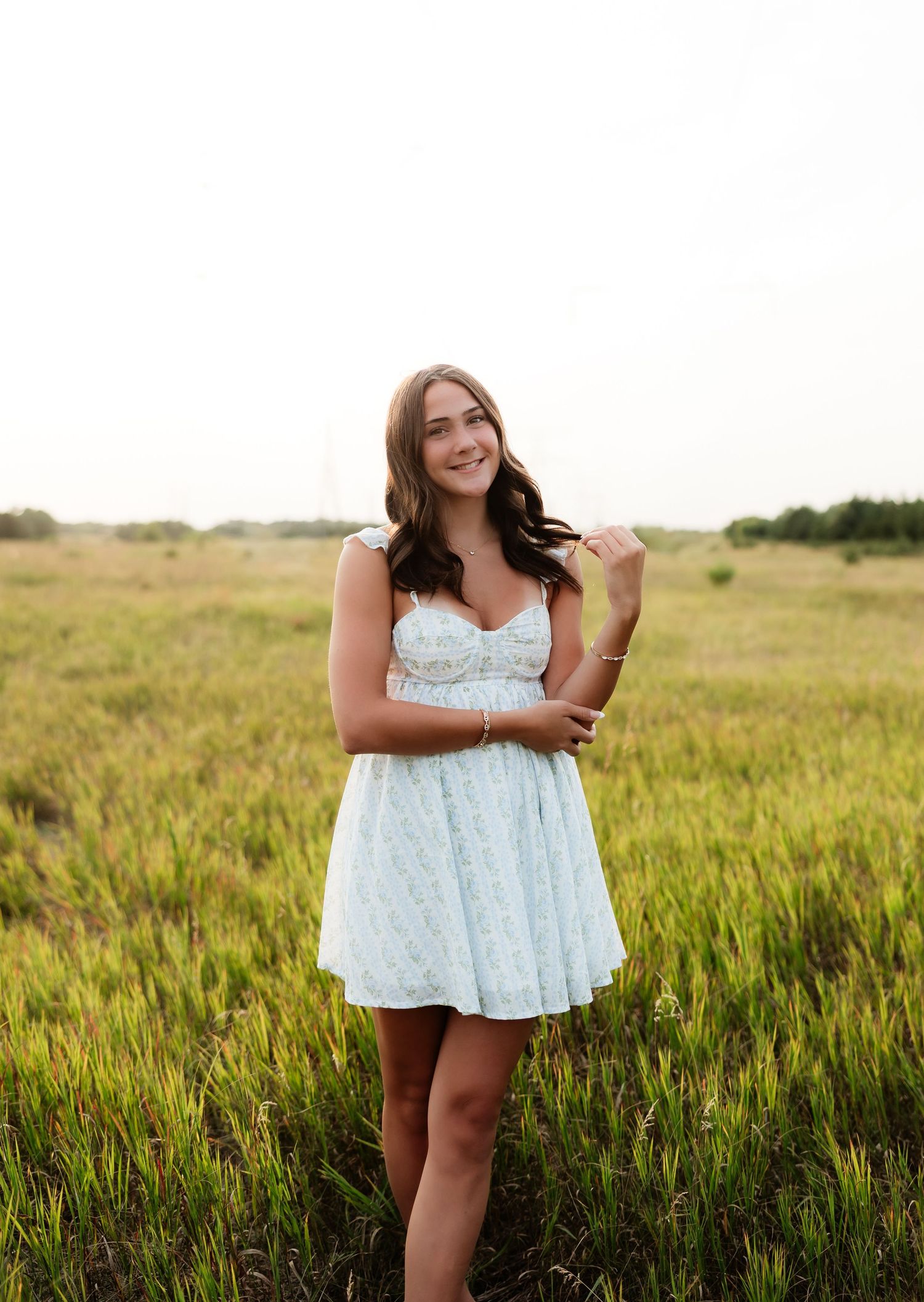 Young woman in light blue mini dress standing in a golden grass meadow under soft sky.