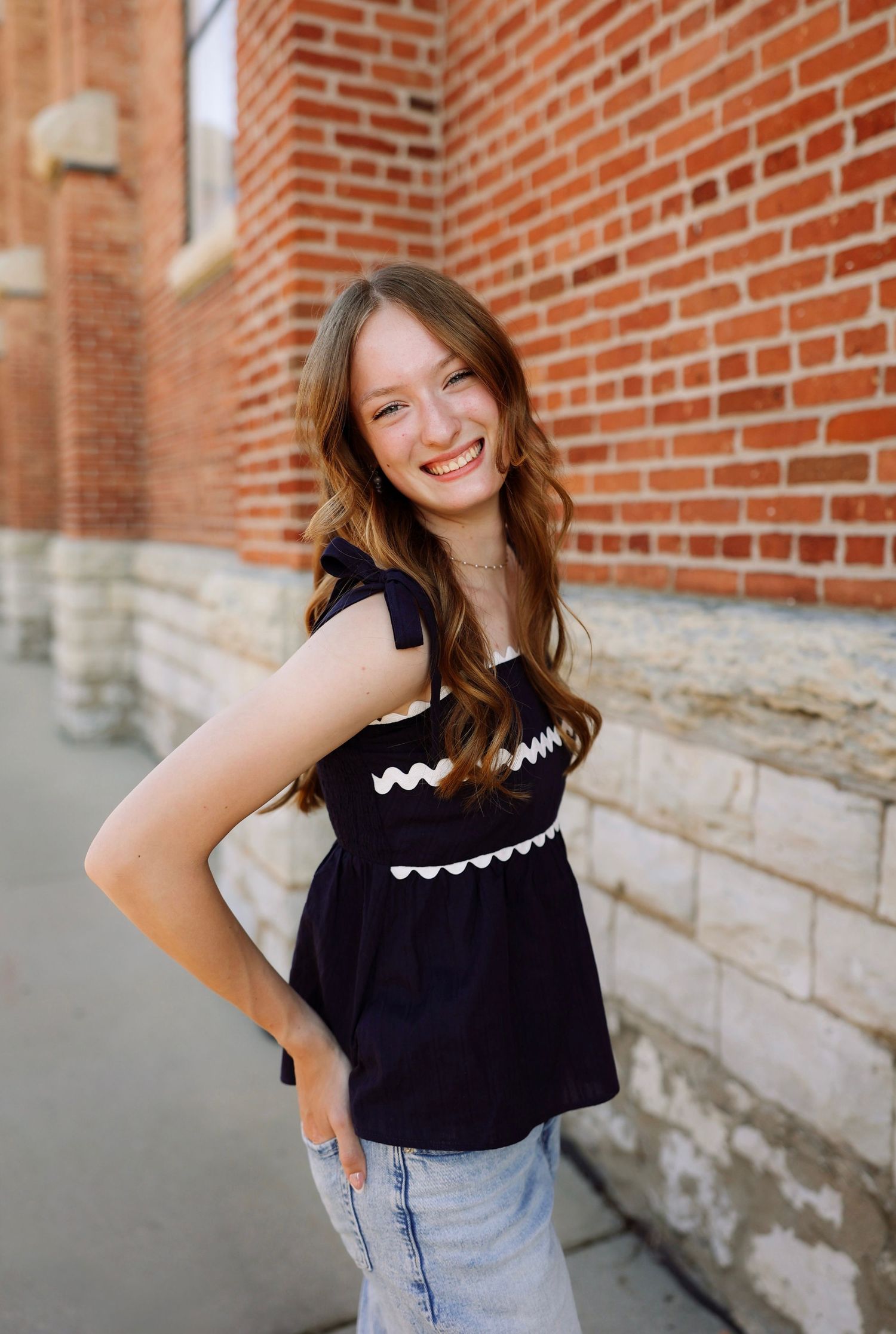 Smiling young woman in black top with white trim posing against a red brick wall outdoors.