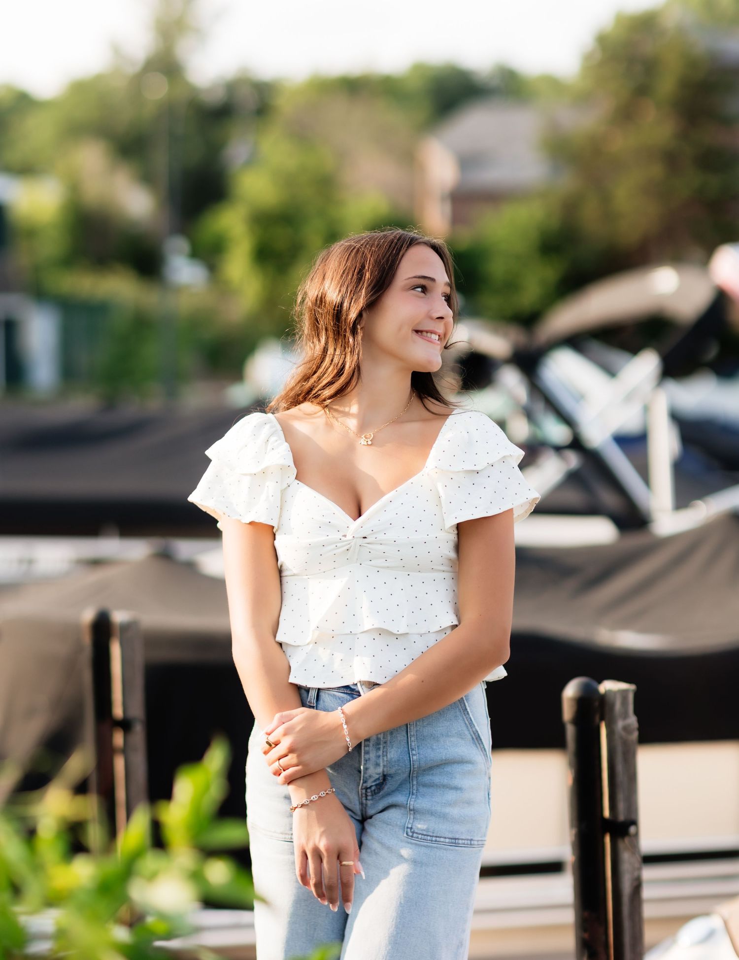 Young woman in white ruffled crop top and jeans smiling outdoors near a marina on a sunny day.