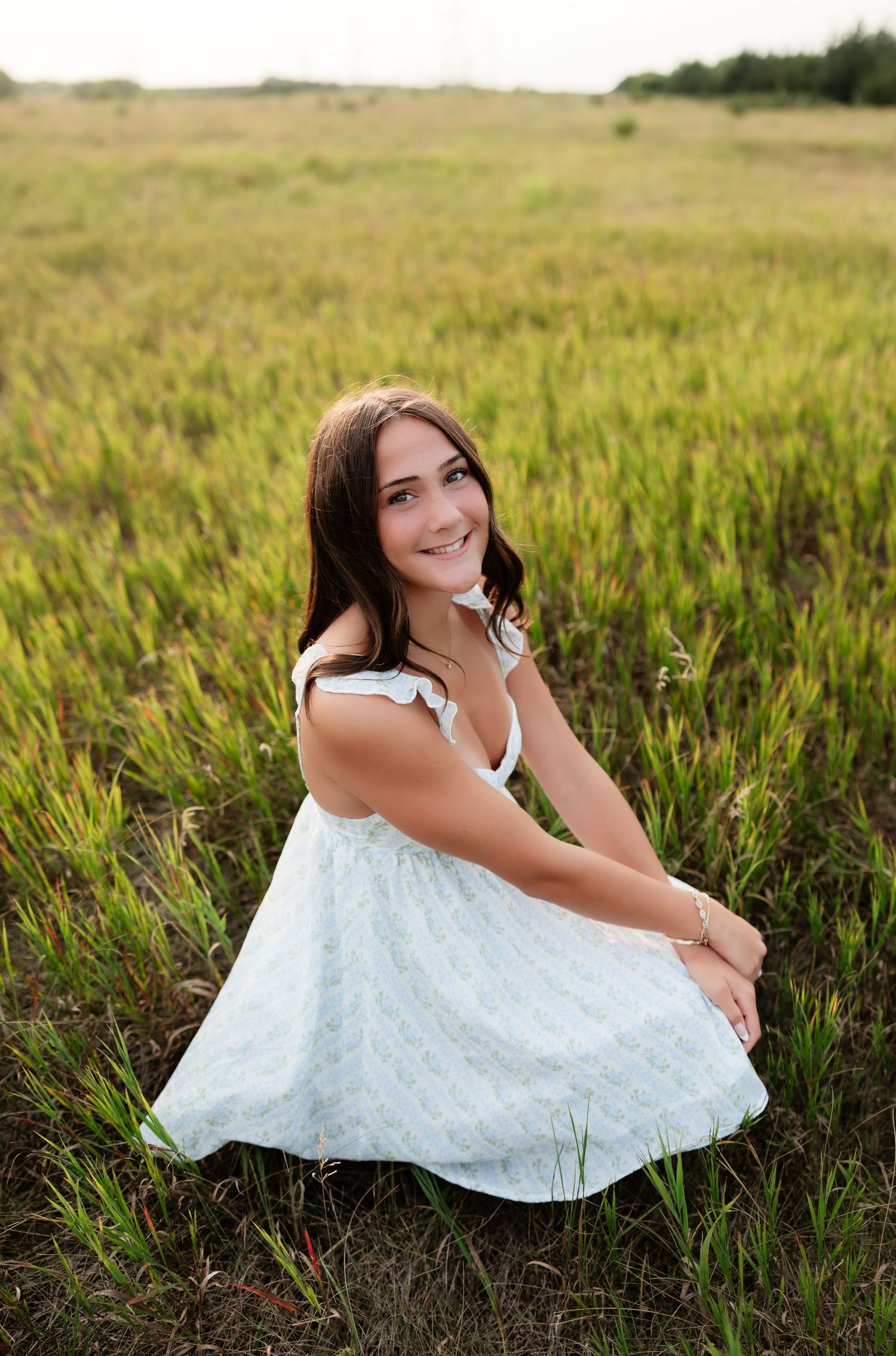 Young woman in white dress crouching in a green grassy meadow.