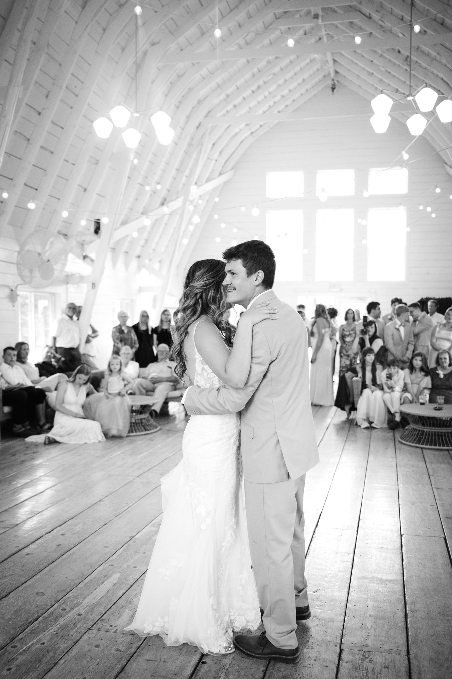 Black and white photo of bride and groom sharing their first dance in a rustic barn venue.