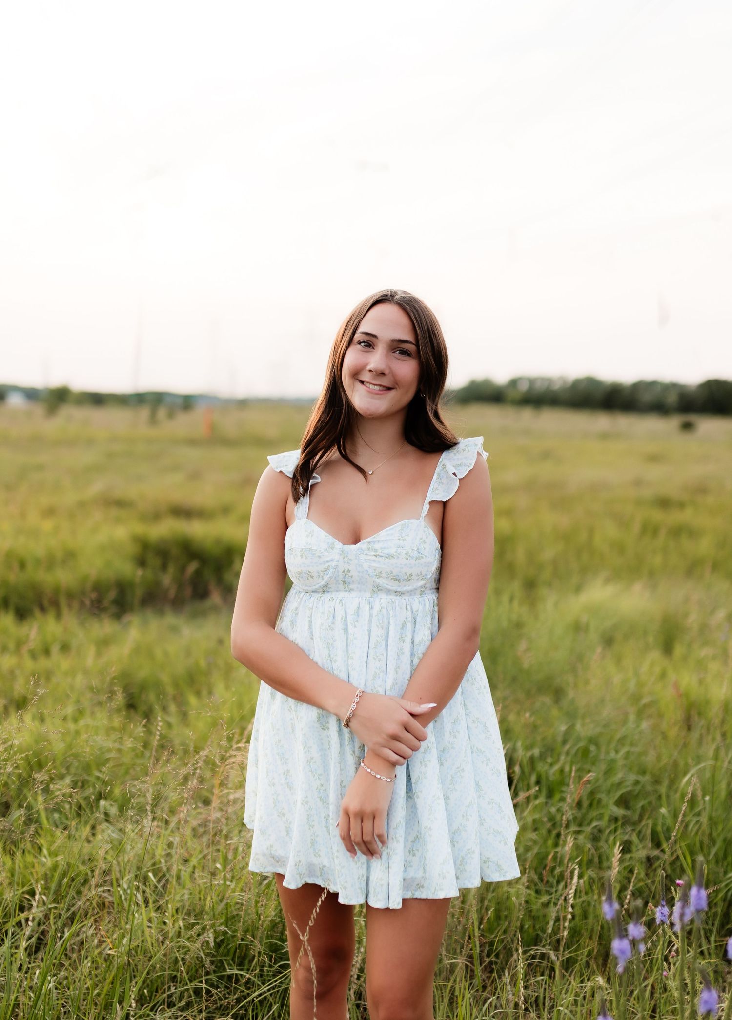 Smiling brunette in light blue ruffled dress posing in green meadow field.