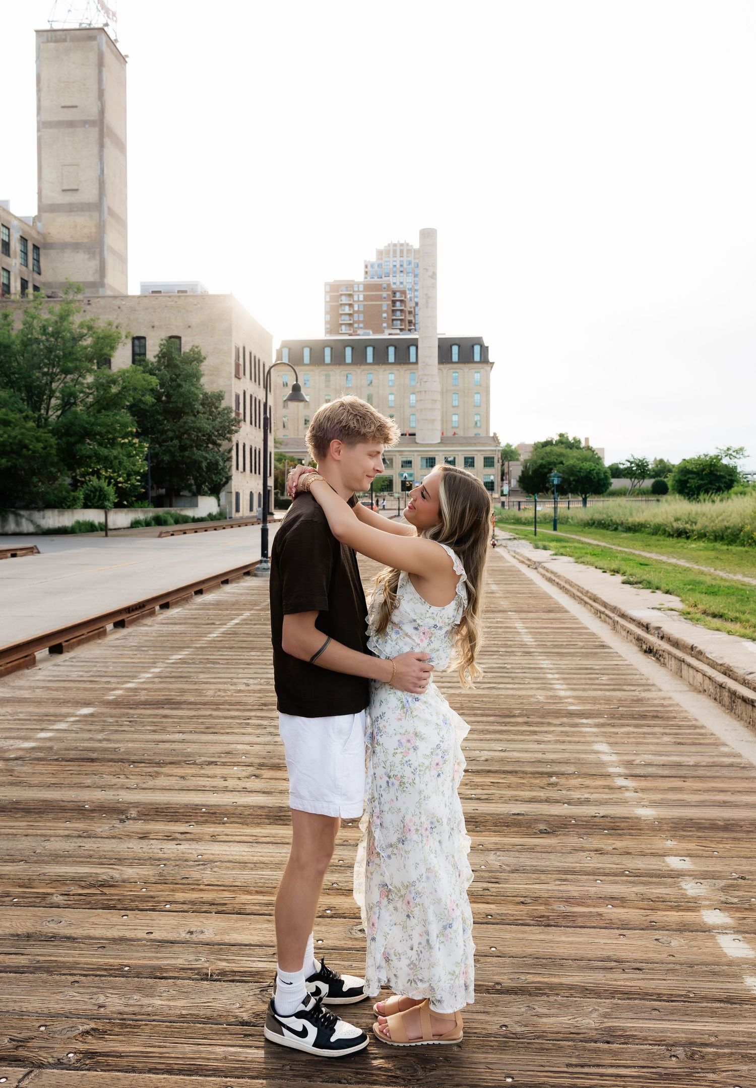 Young couple embracing and almost kissing on urban railroad tracks with city buildings in background.