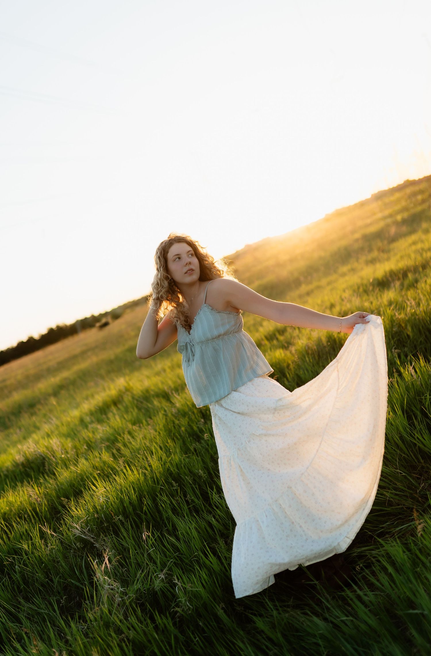 Young woman in flowing white skirt twirling in green field at golden sunset.