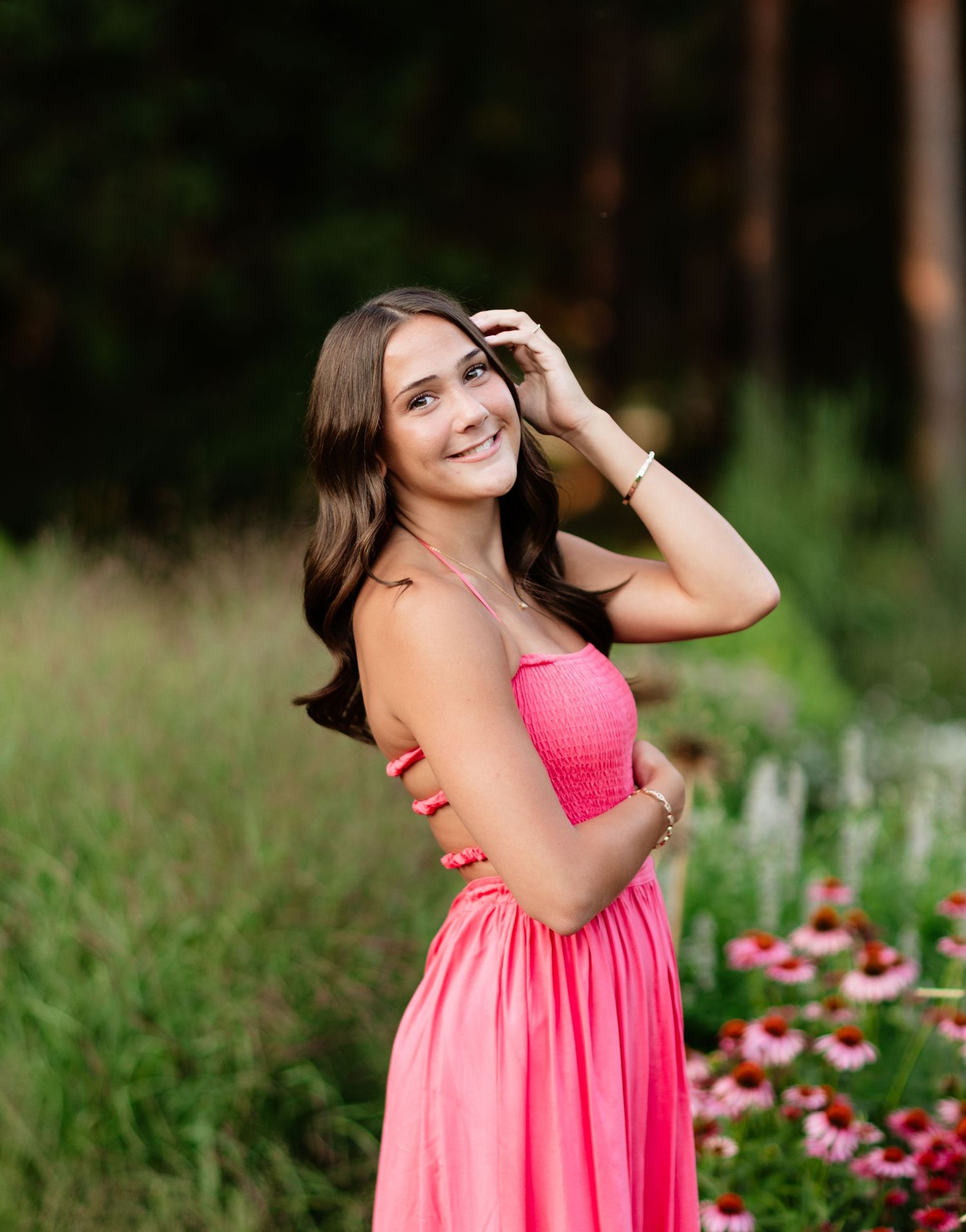 Happy young woman in pink dress posing among wildflowers in a sun-drenched outdoor setting.