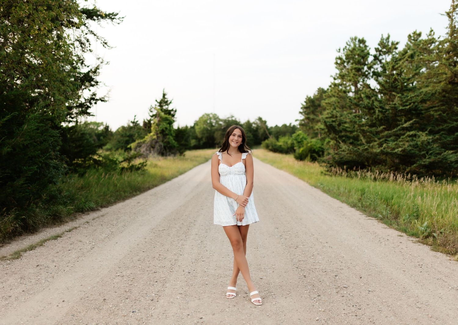 Young woman in white dress walking on scenic gravel road surrounded by greenery.
