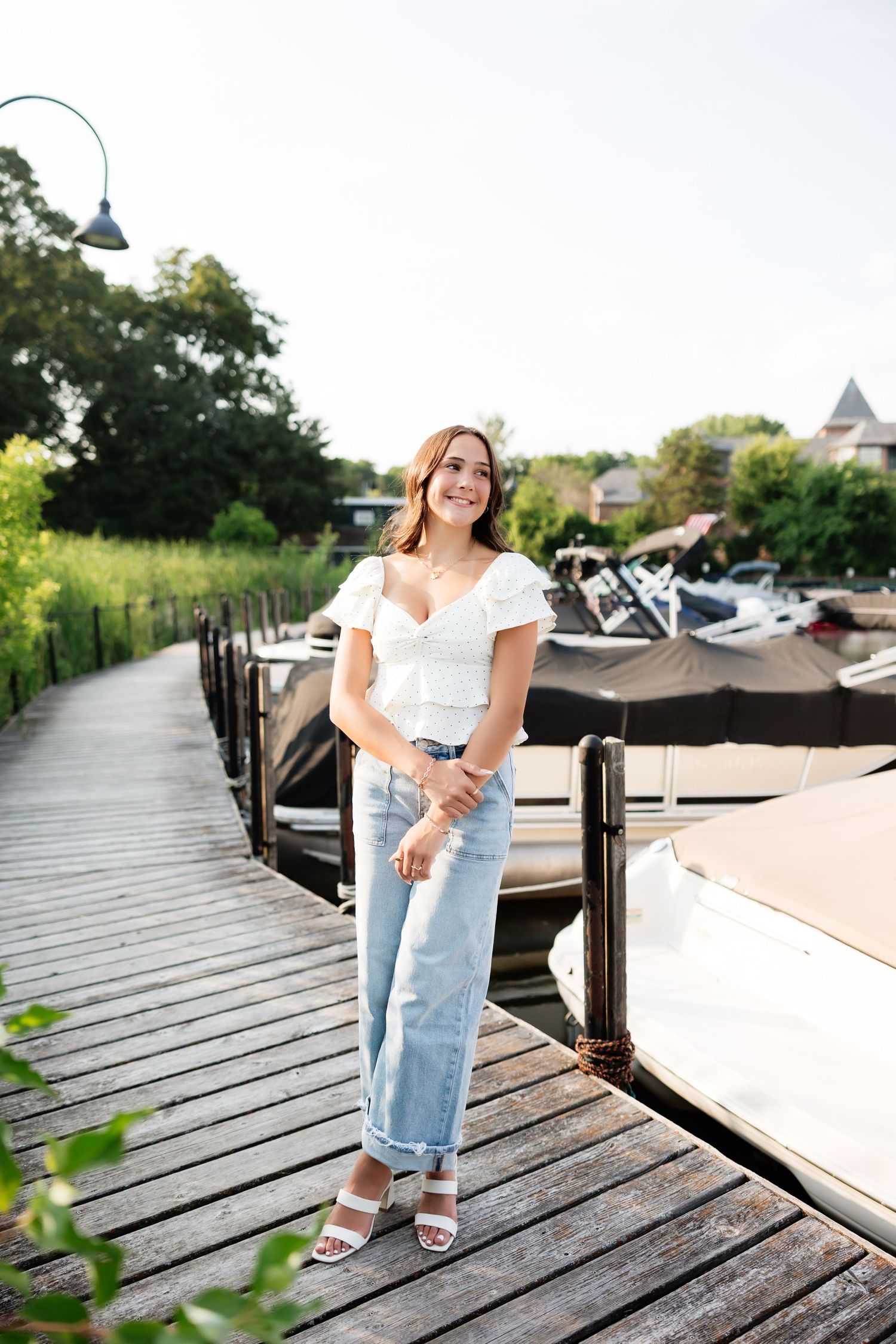 Smiling young woman in white top and light jeans standing on wooden marina dock on sunny day.