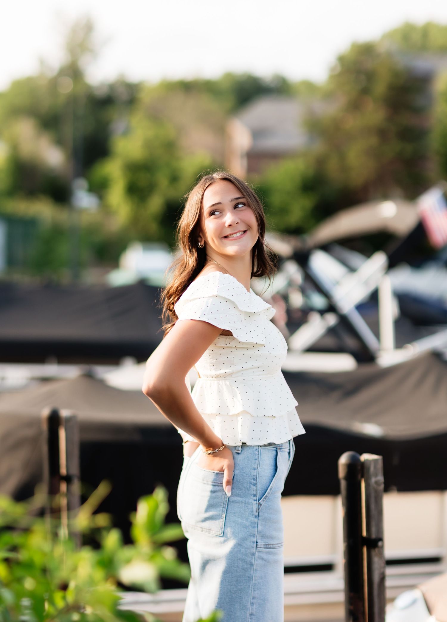 Young woman in white ruffled top and jeans smiling over shoulder outdoors.