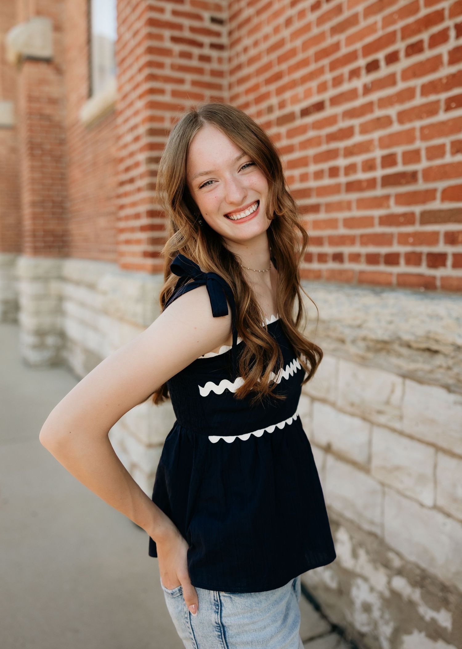 Smiling young woman in black top with white trim poses against a red brick wall outdoors.