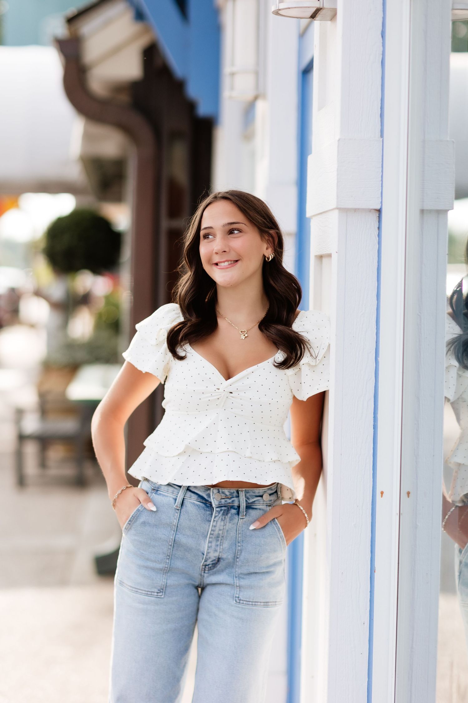 Young woman in white crop top and light jeans leaning against blue and white building outdoors.