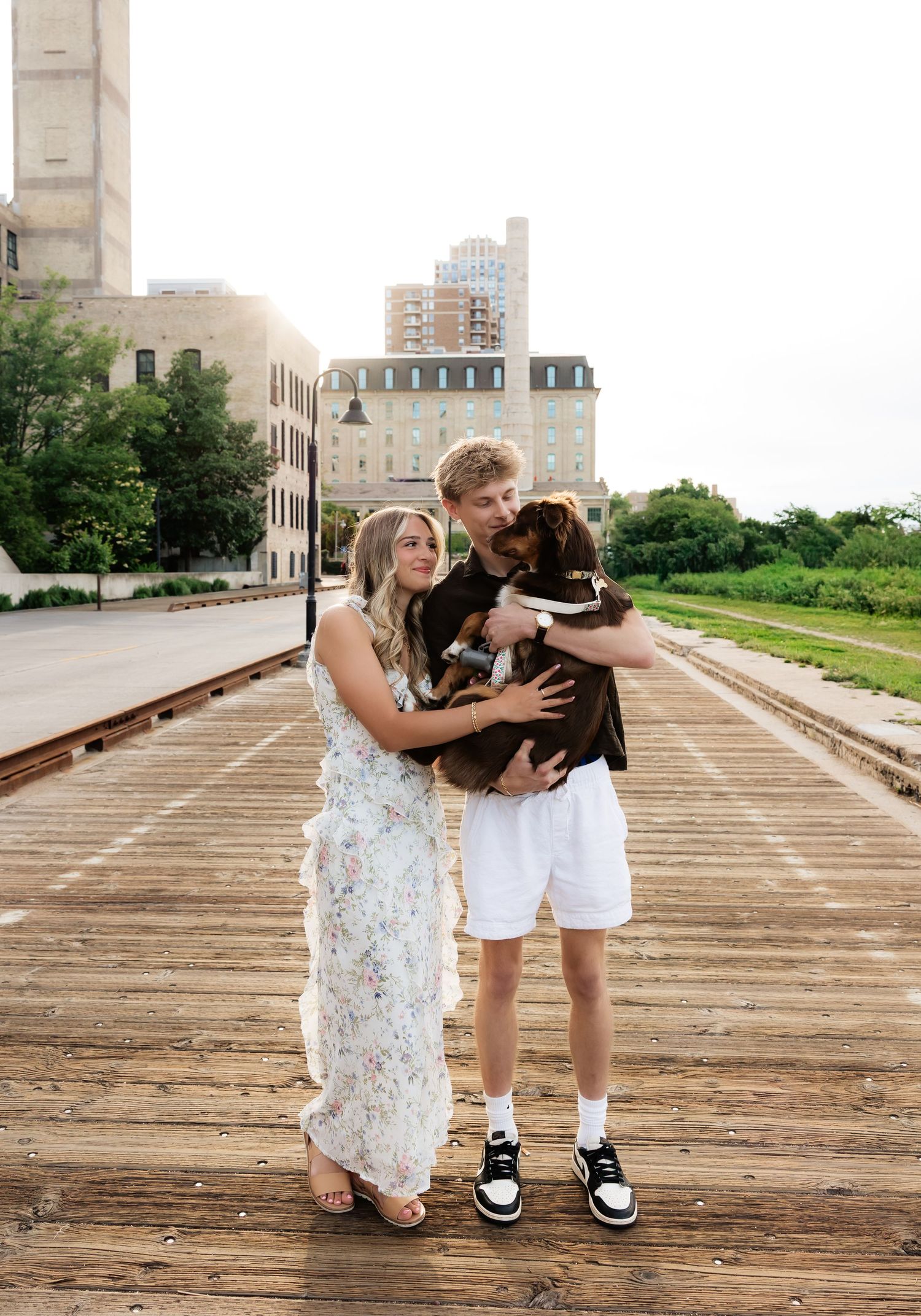 Couple holding their brown dog on a wooden bridge with urban buildings in the background.